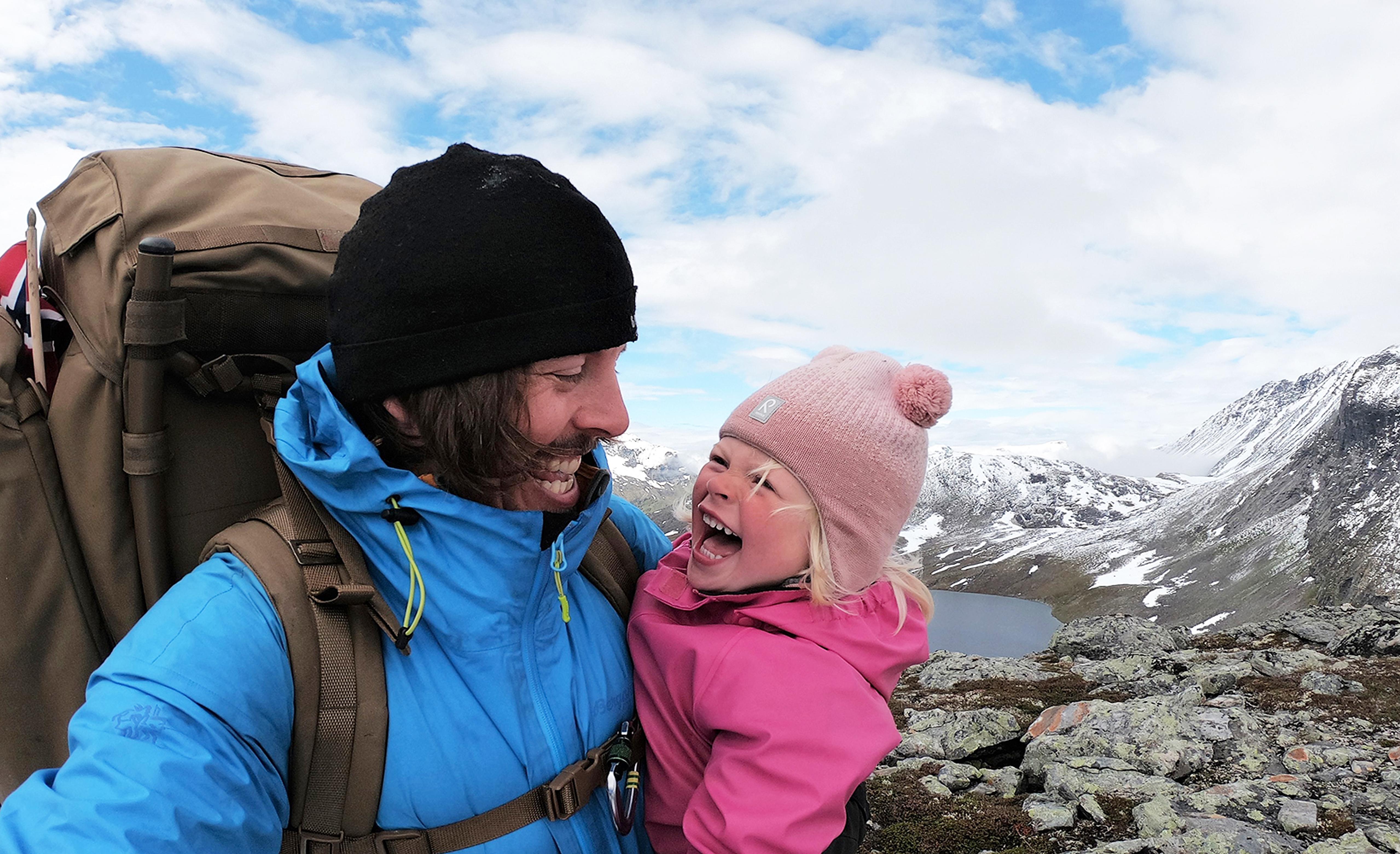 En lille pige og hendes far smiler og krammer hinanden på en vandretur ved Hjørundfjorden i Fjord Norge