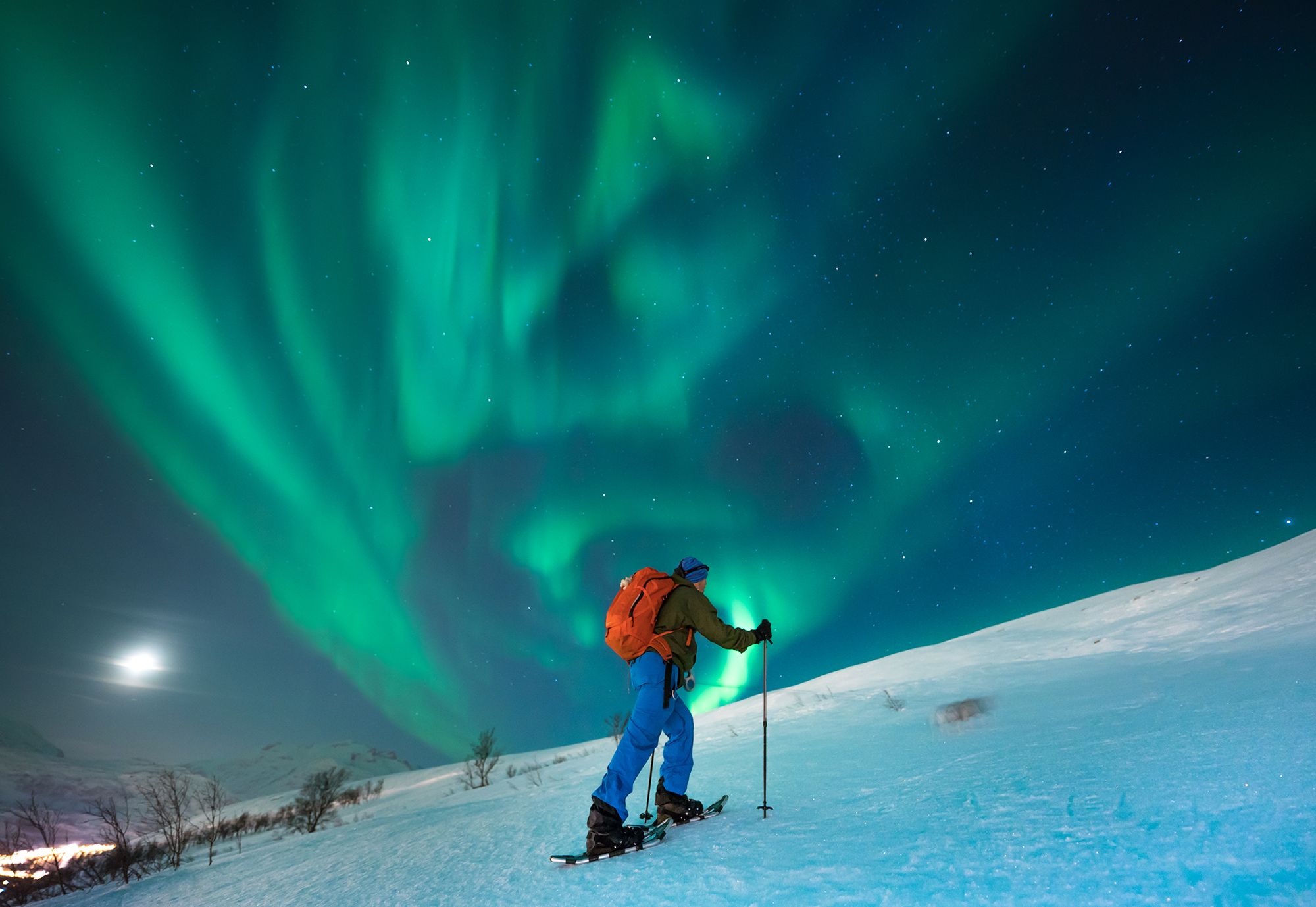 A person snowshoeing under the northern lights in Tromsø, Northern Norway