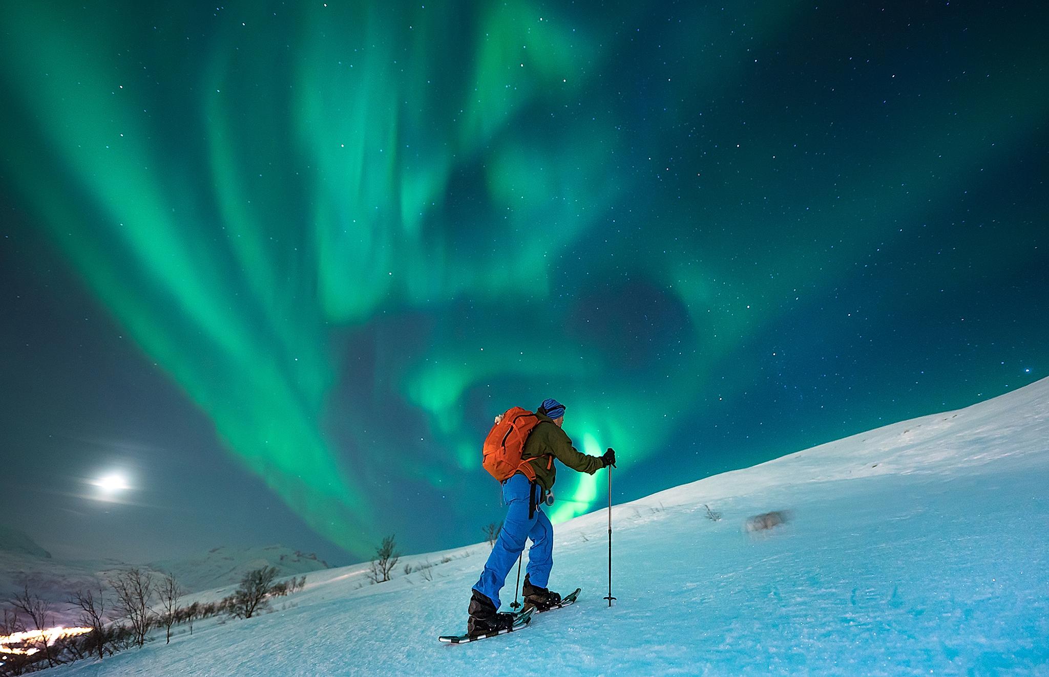 A person snowshoeing under the northern lights in Tromsø, Northern Norway