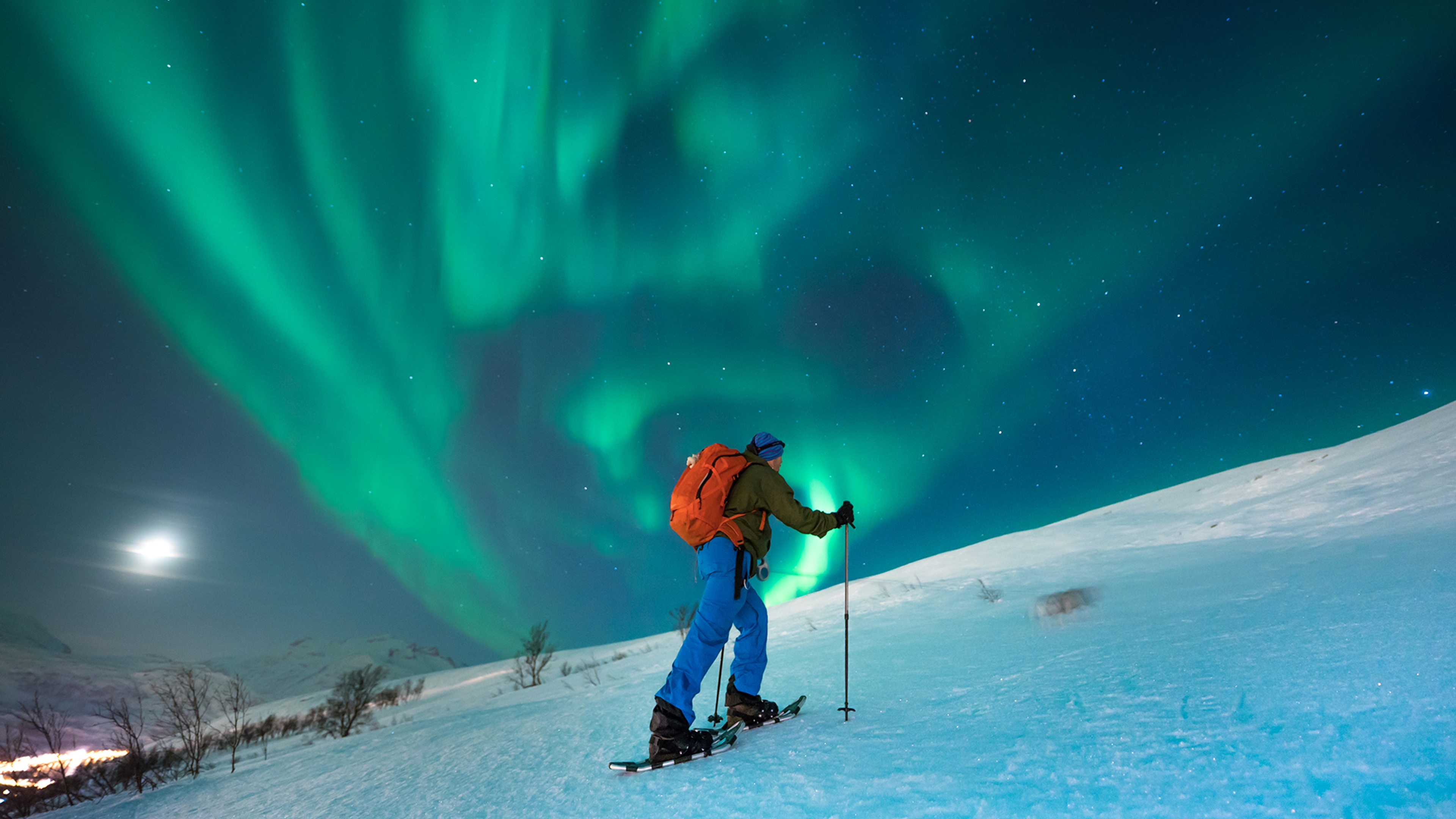 A person snowshoeing under the northern lights in Tromsø, Northern Norway