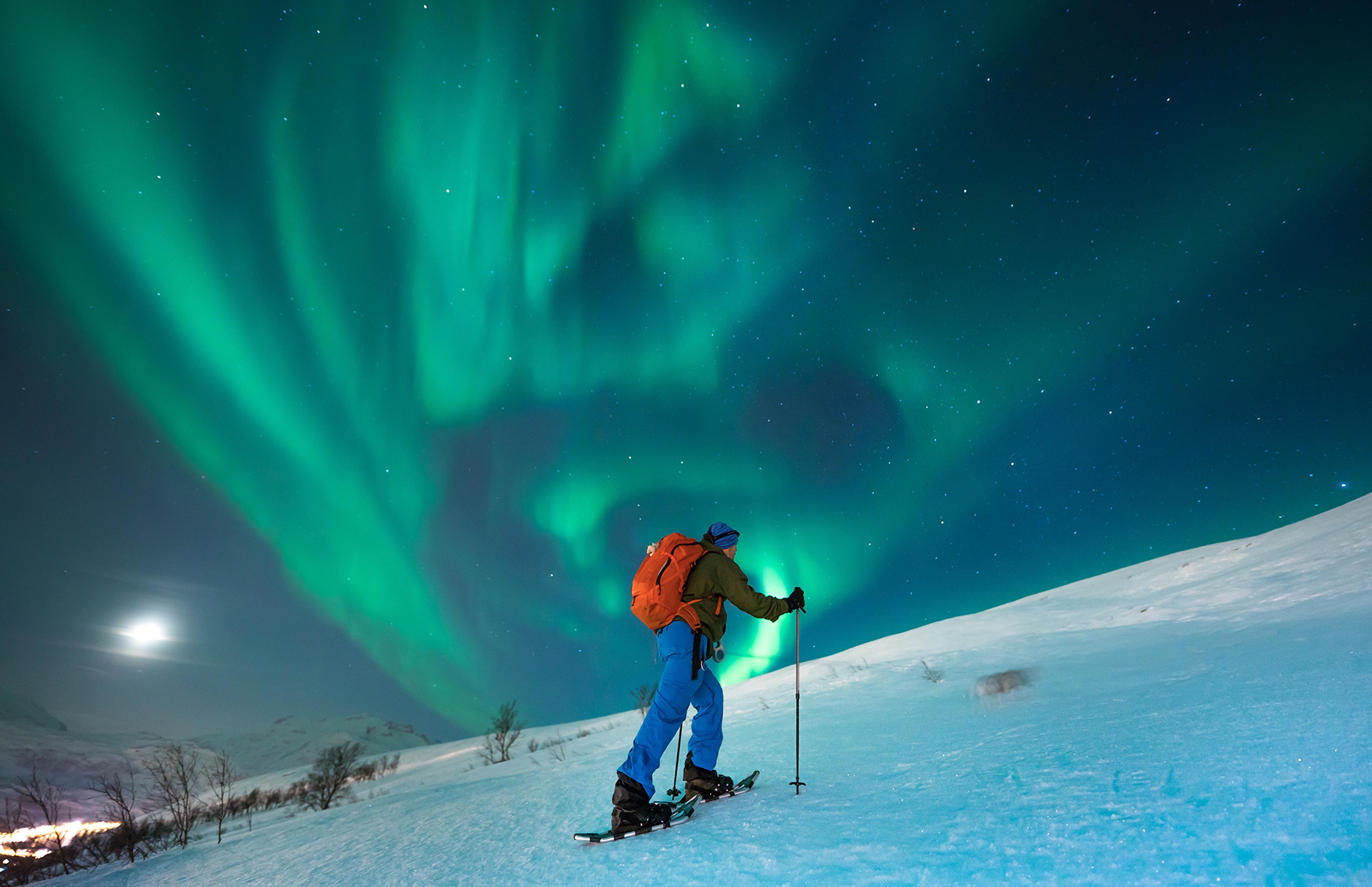 A person snowshoeing under the northern lights in Tromsø, Northern Norway