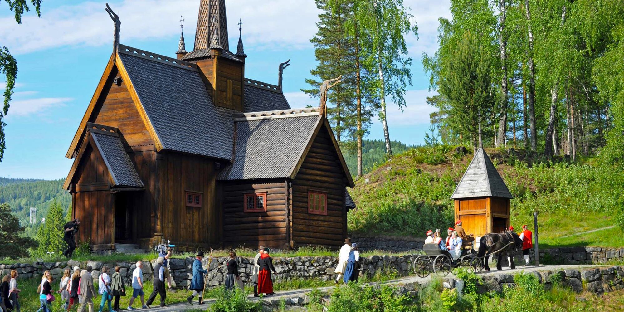 Groupe de personnes en costume traditionnel passant devant l’église en bois debout à Maihaugen à Lillehammer, en Norvège de l'Est