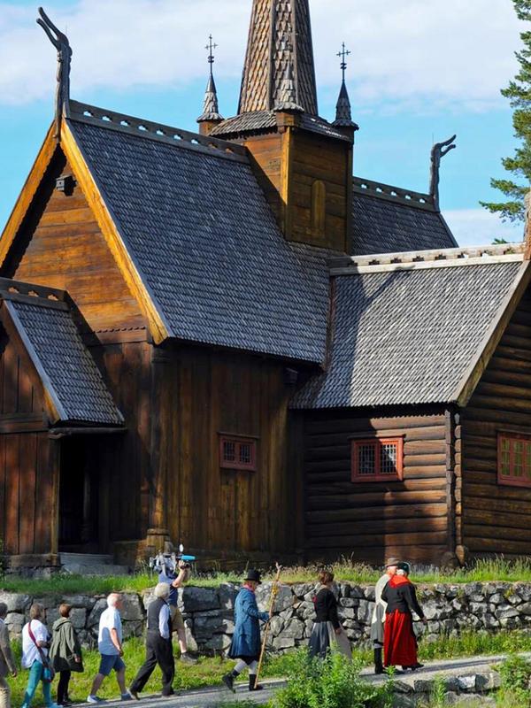 Groupe de personnes en costume traditionnel passant devant l’église en bois debout à Maihaugen à Lillehammer, en Norvège de l'Est