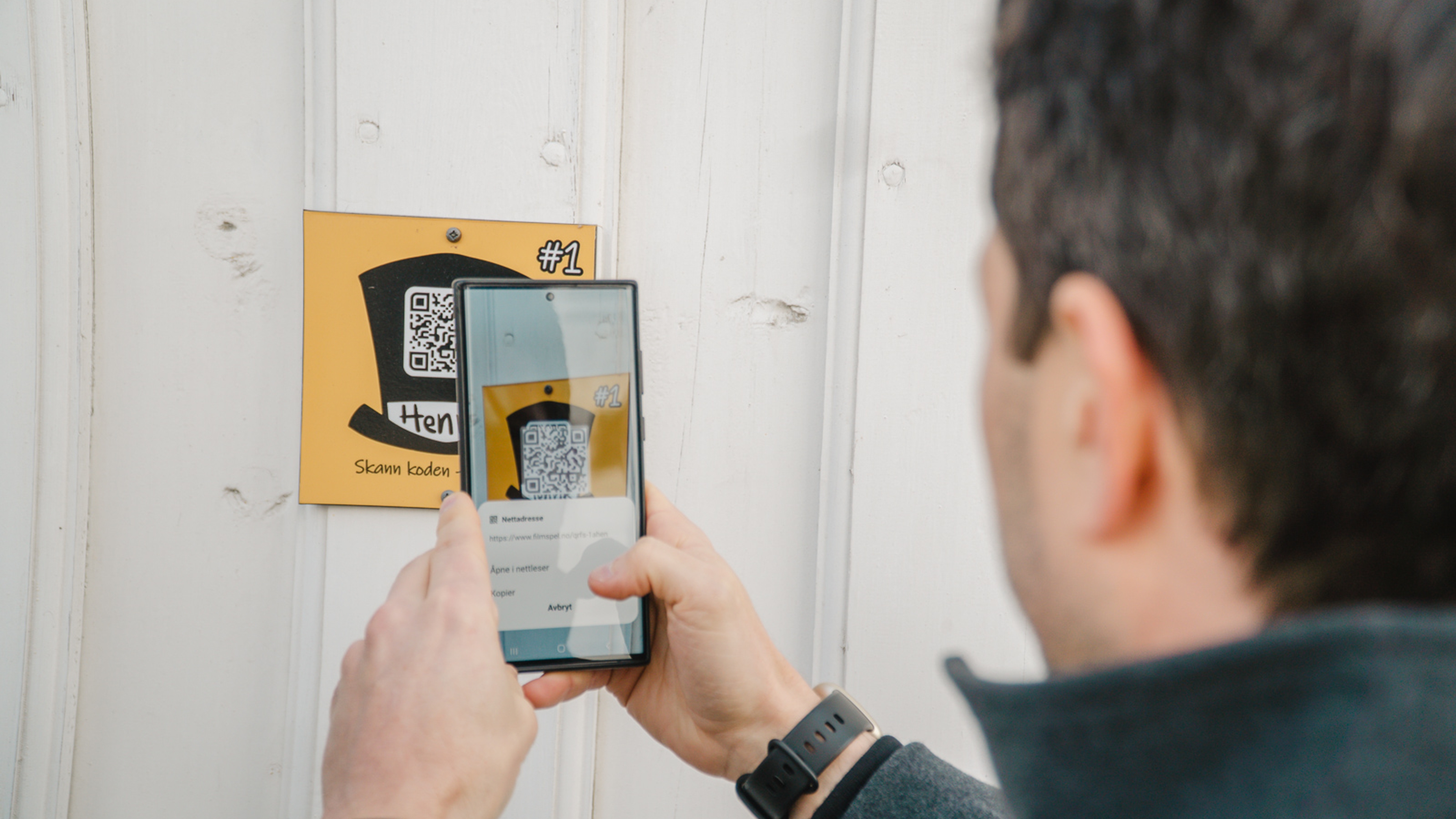 A man scanning a QR-code at a wall in Grimstad, Southern Norway.