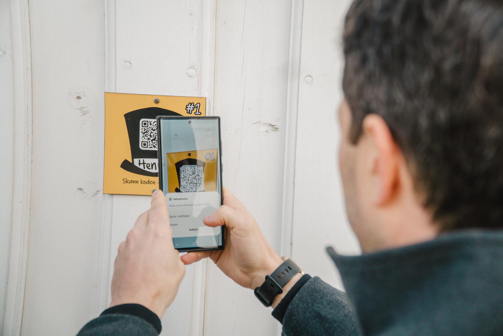 A man scanning a QR-code at a wall in Grimstad, Southern Norway.