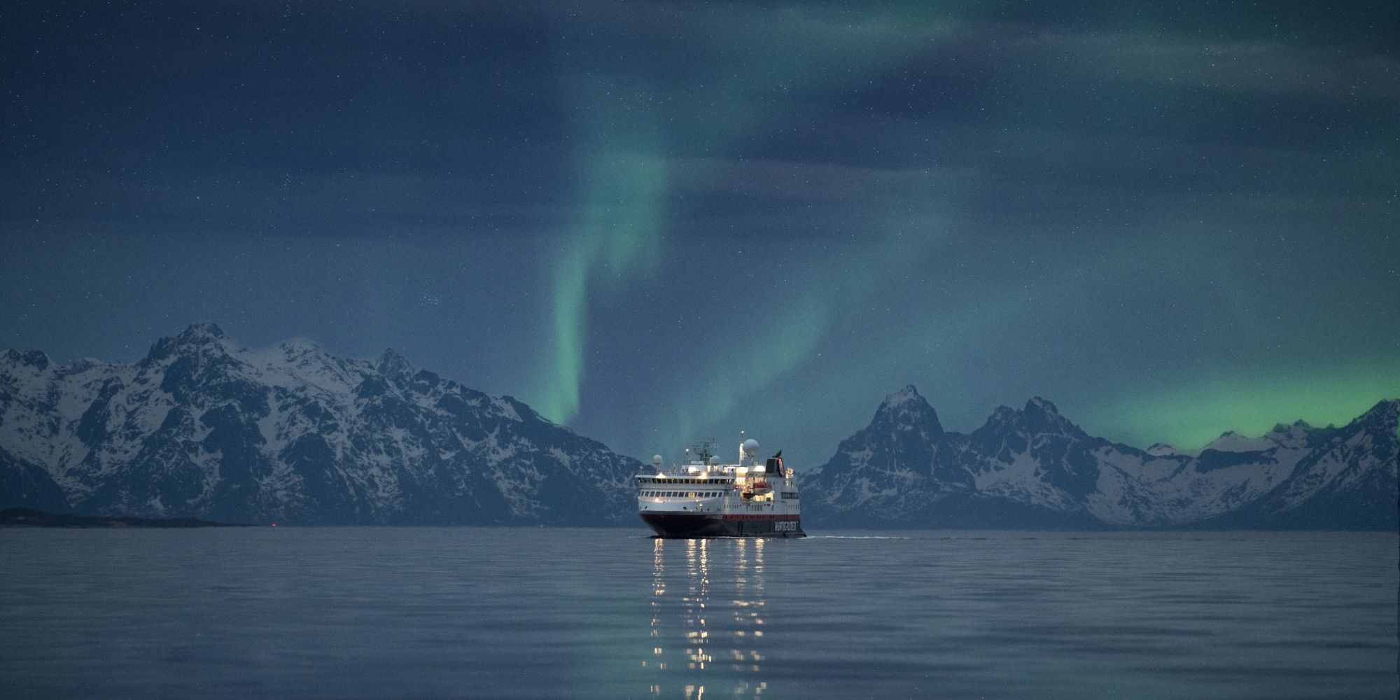 The northern lights dancing across the Arctic sky as Hurtigruten sails below in Northern Norway
