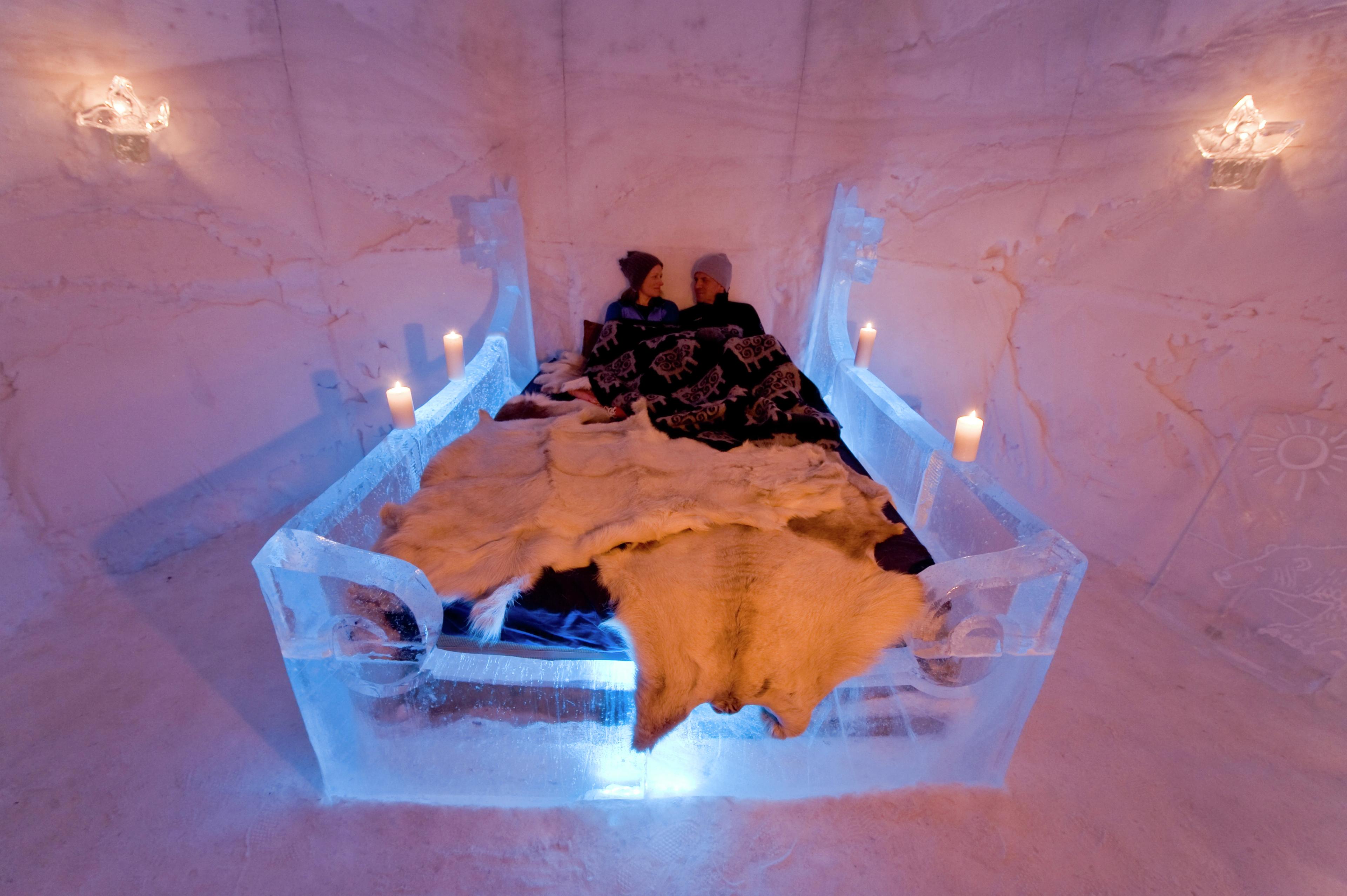 Two people in a bed with reindeer blankets in Sorrisniva Igloo Hotel, Northern Norway