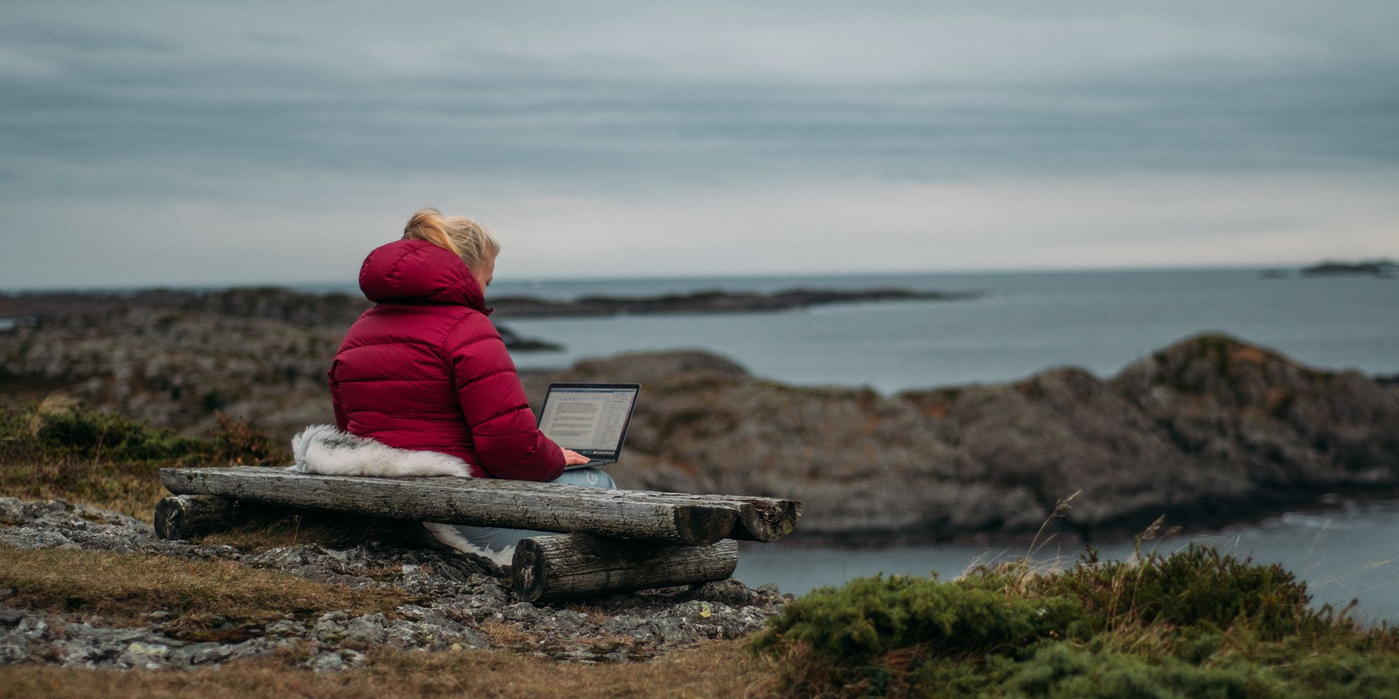 A woman sitting outdoors with her computer in Solund in Fjord Norway
