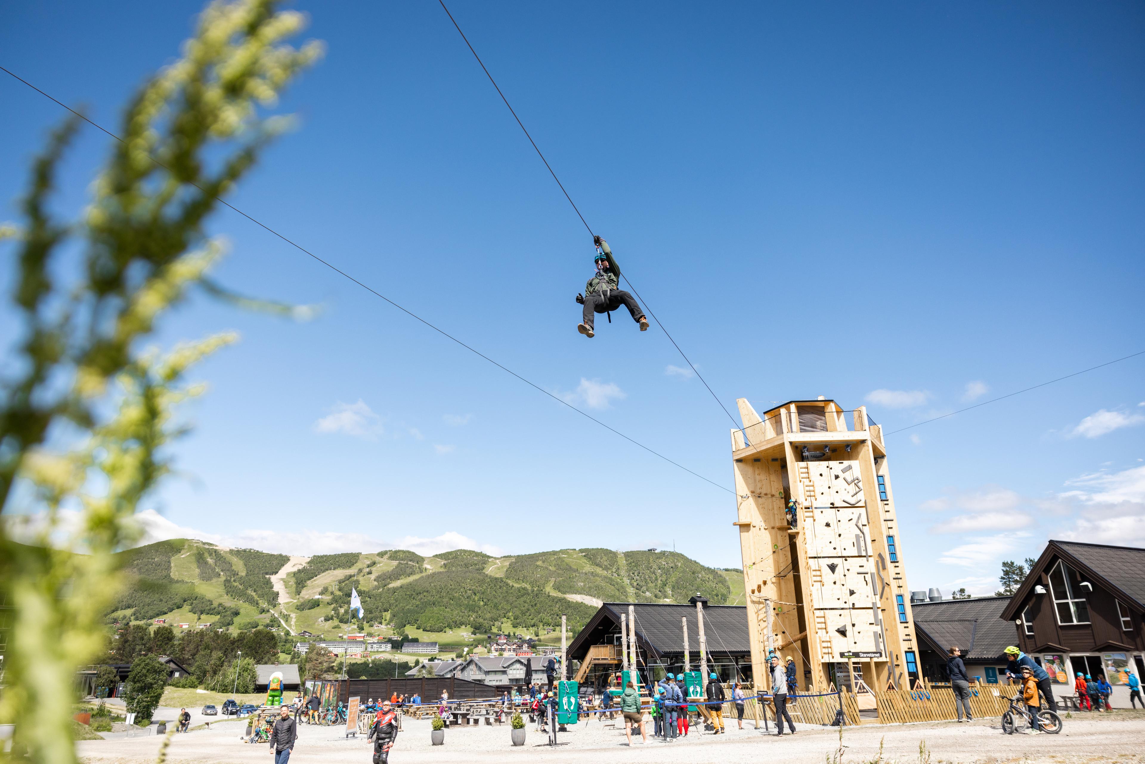 Person zip lining down from Skarvetårnet climbing tower in Geilo Summer Park, Eastern Norway