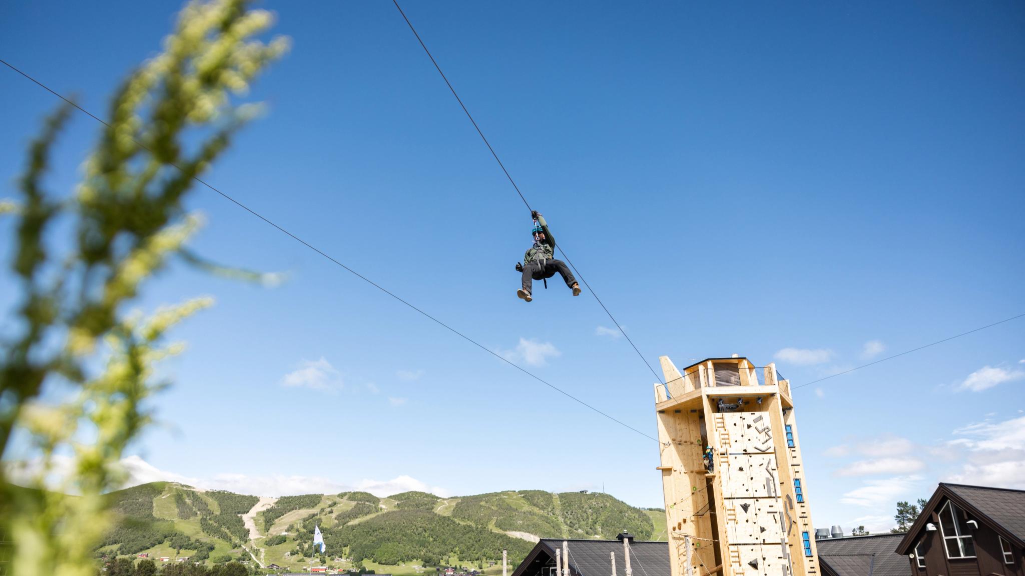 Person zip lining down from Skarvetårnet climbing tower in Geilo Summer Park, Eastern Norway
