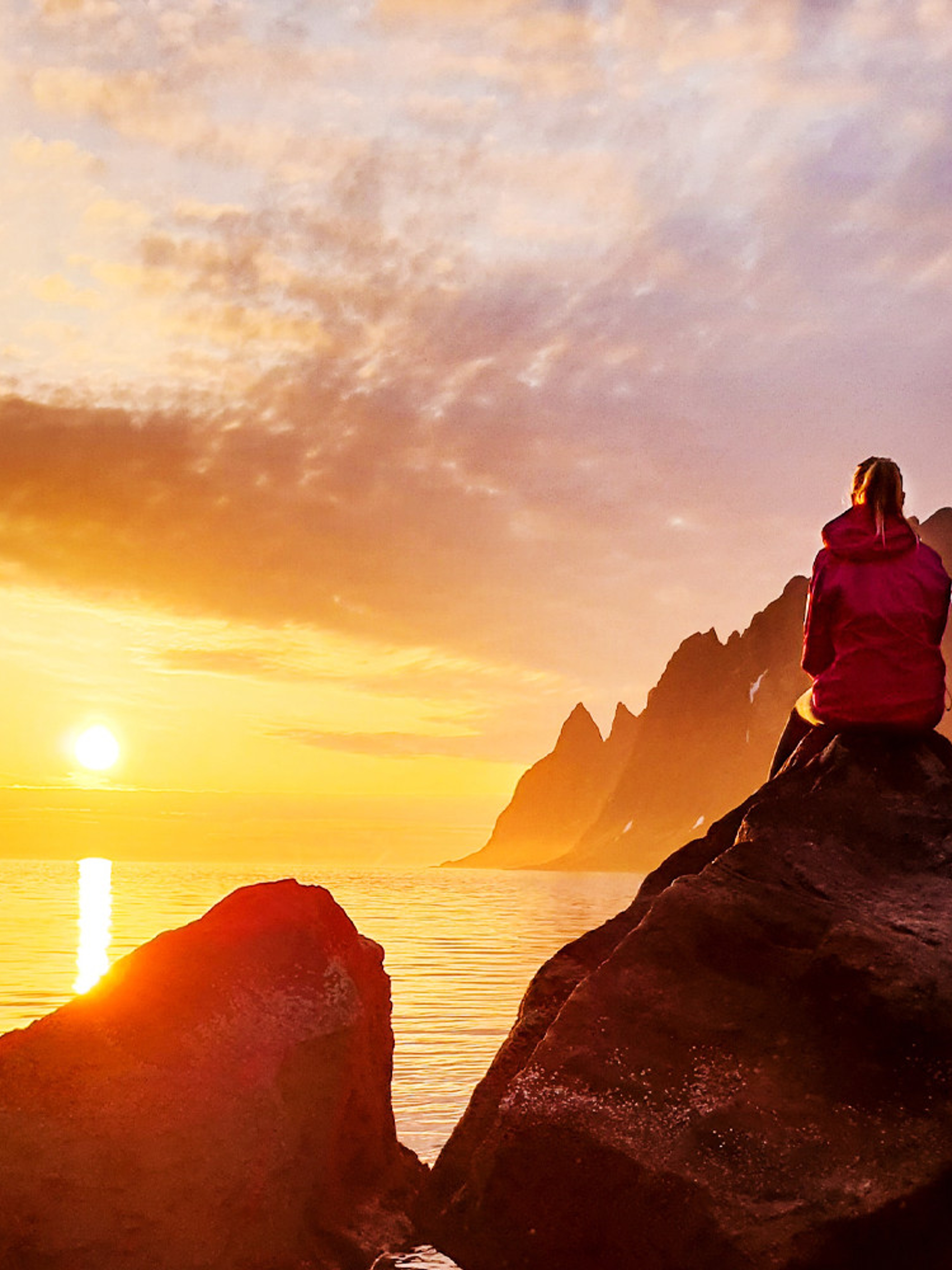 Eine Person beobachtet die Mitternachtssonne bei Senja in Nordnorwegen