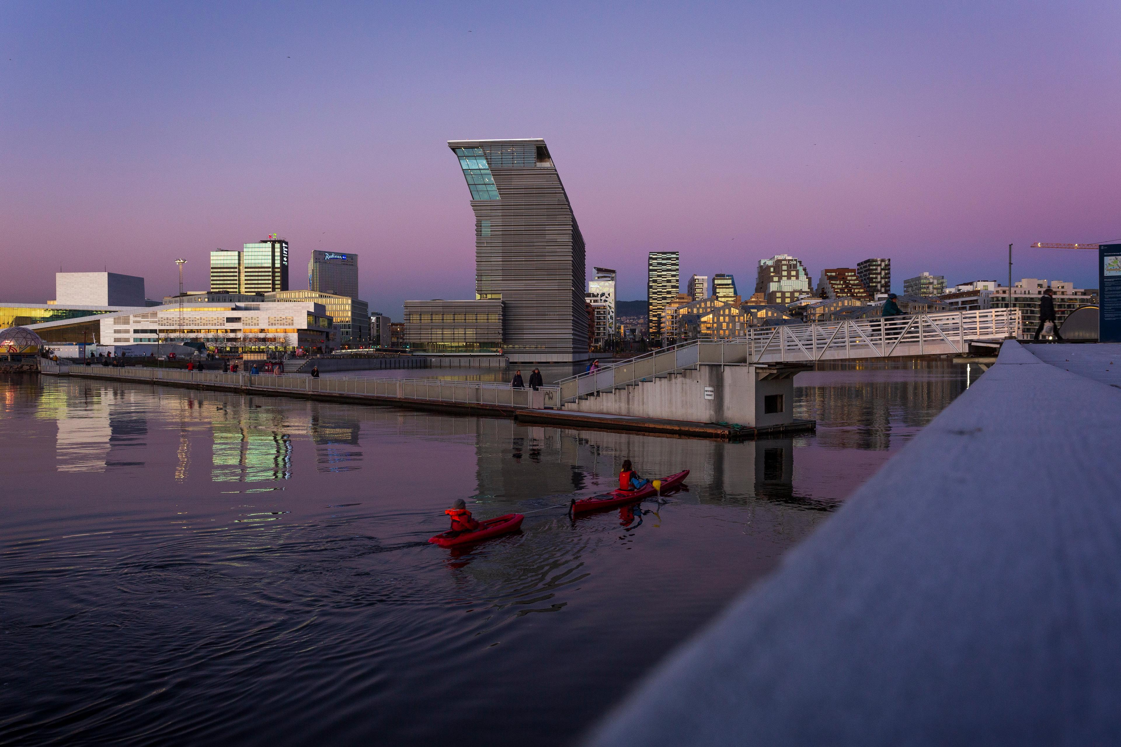 Two people in kayaks in front of the new Deichman main library in Oslo in a purple sunset