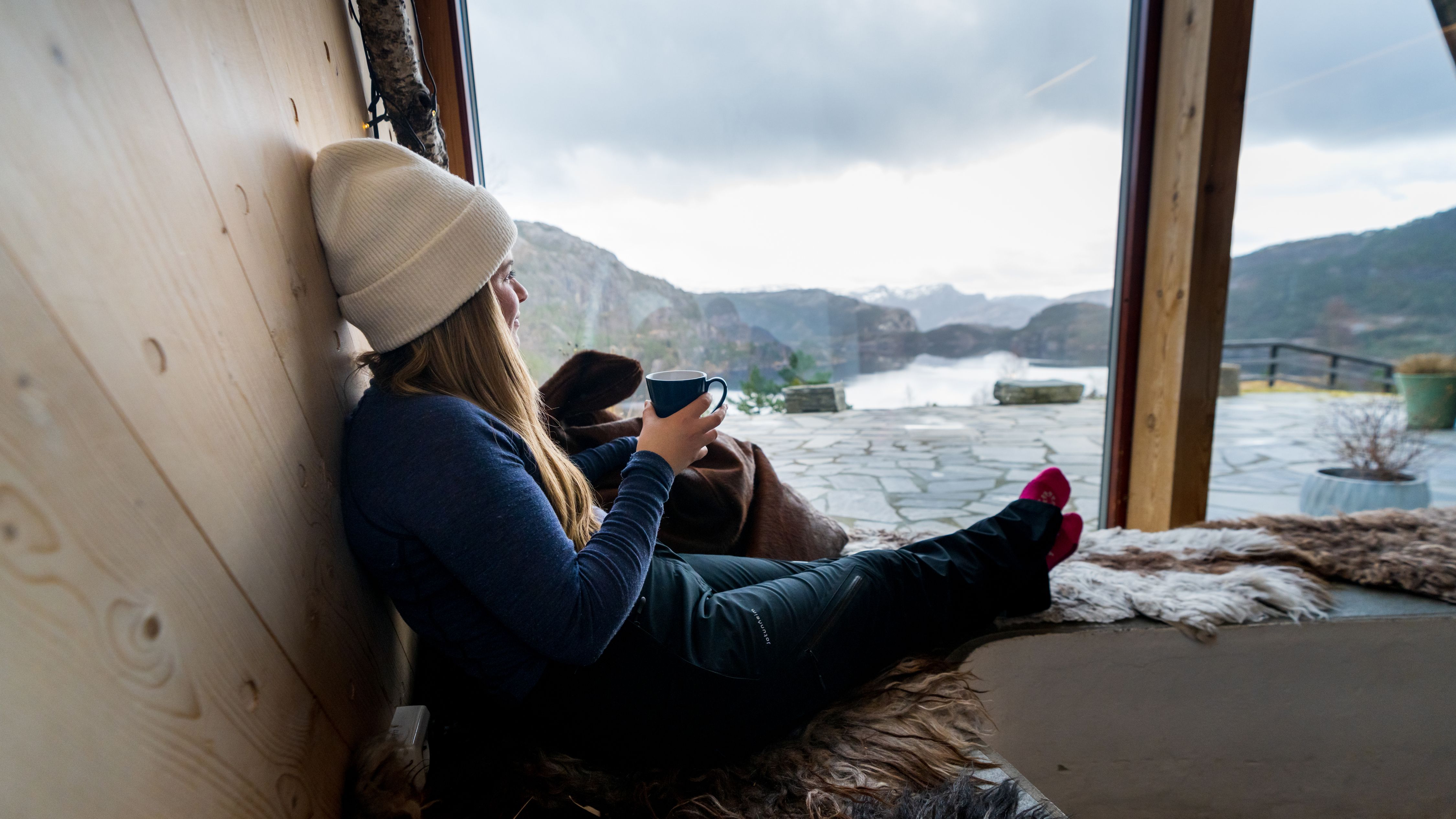 A woman enjoying a coffee while looking out over Refsvatnet from Preikestolen Fjellstue