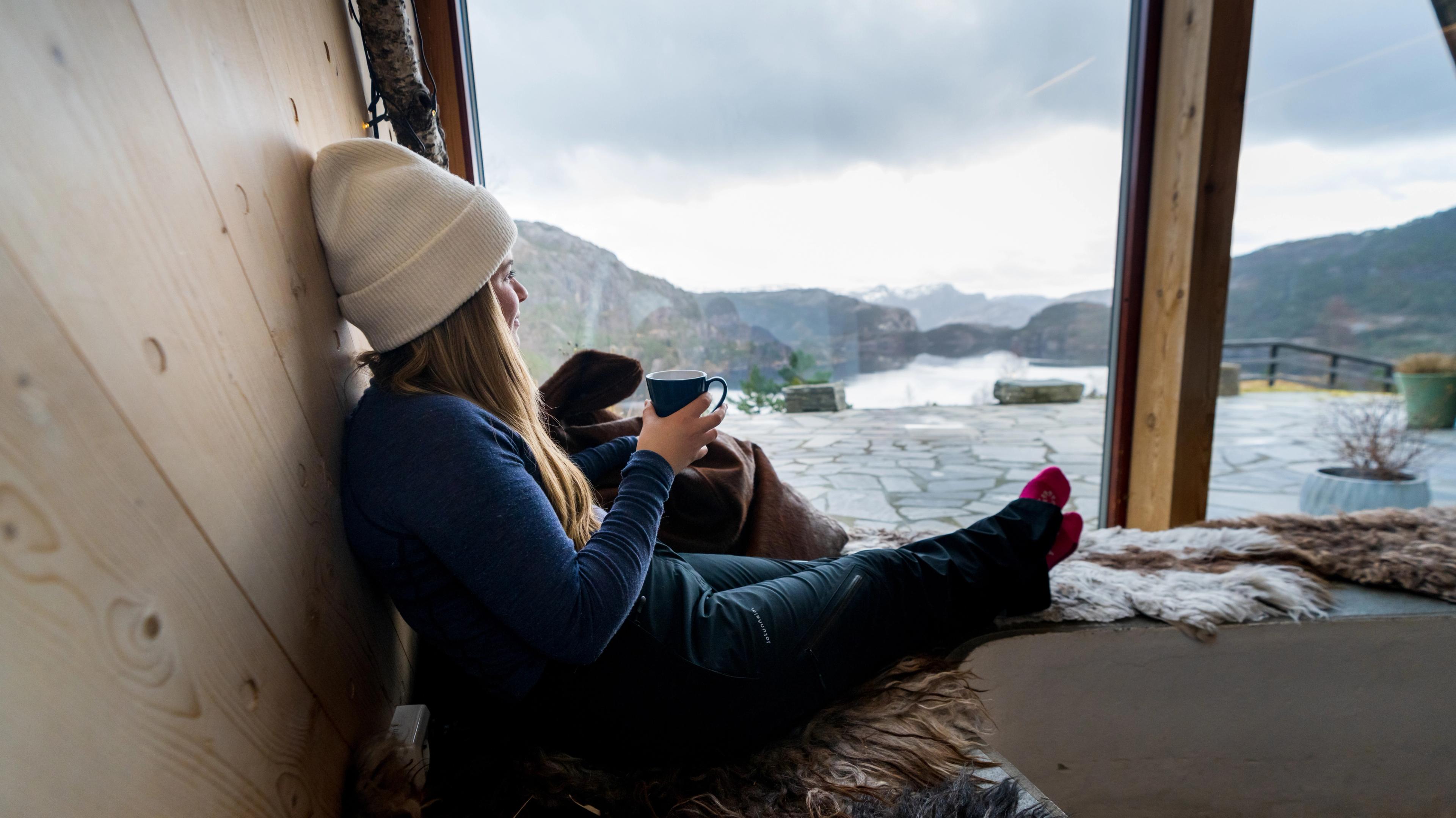 A woman enjoying a coffee while looking out over Refsvatnet from Preikestolen Fjellstue