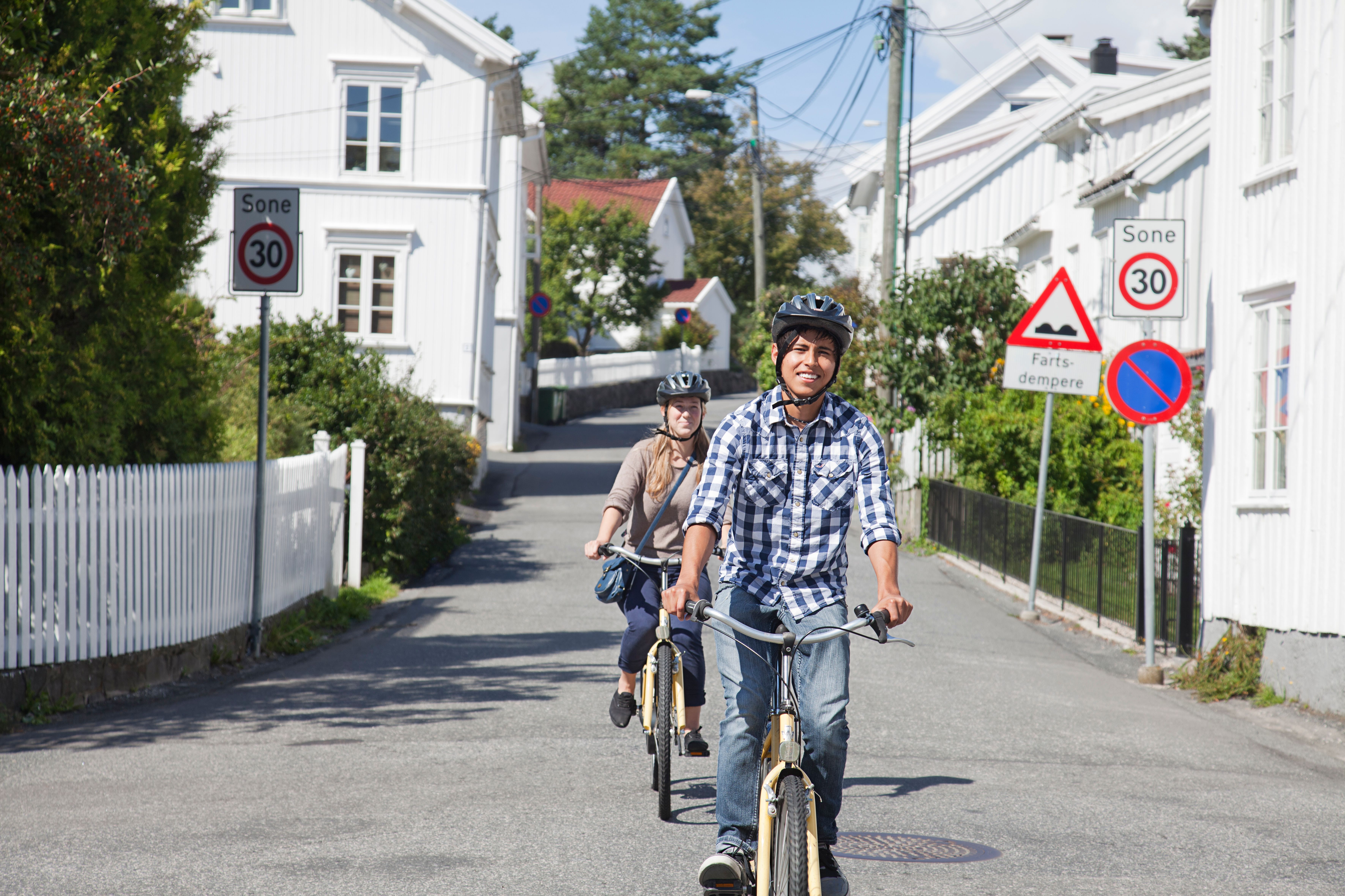To personer sykler forbi hvitmalte hus i Grimstad på Sørlandet