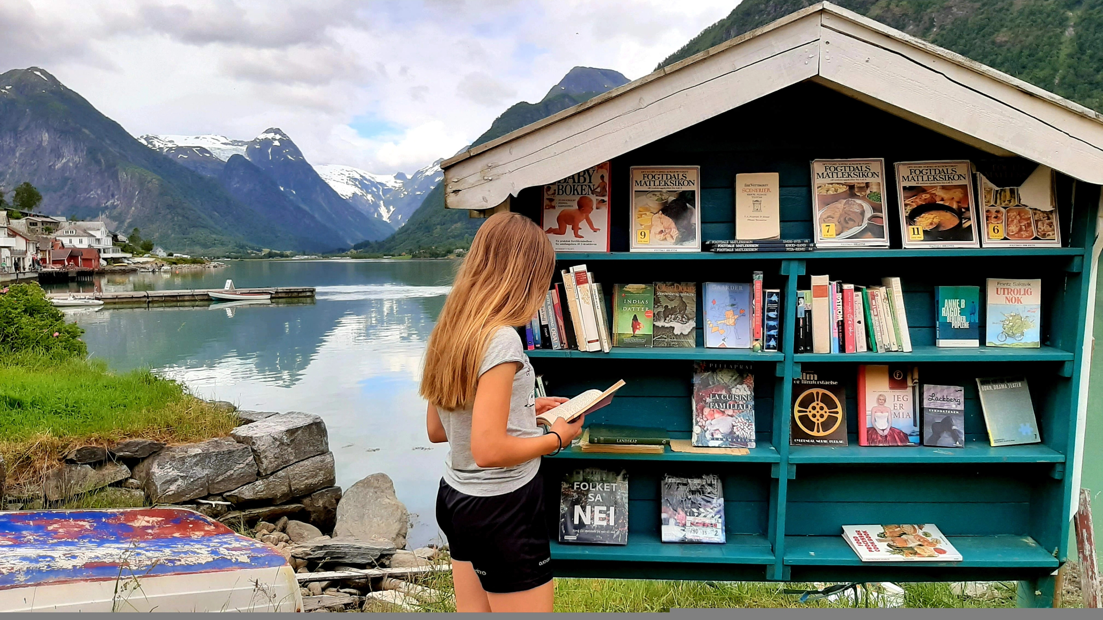 A girl looking at books by an outdoor bookshelf in Fjærland in Fjord Norway, one of Norway's book towns