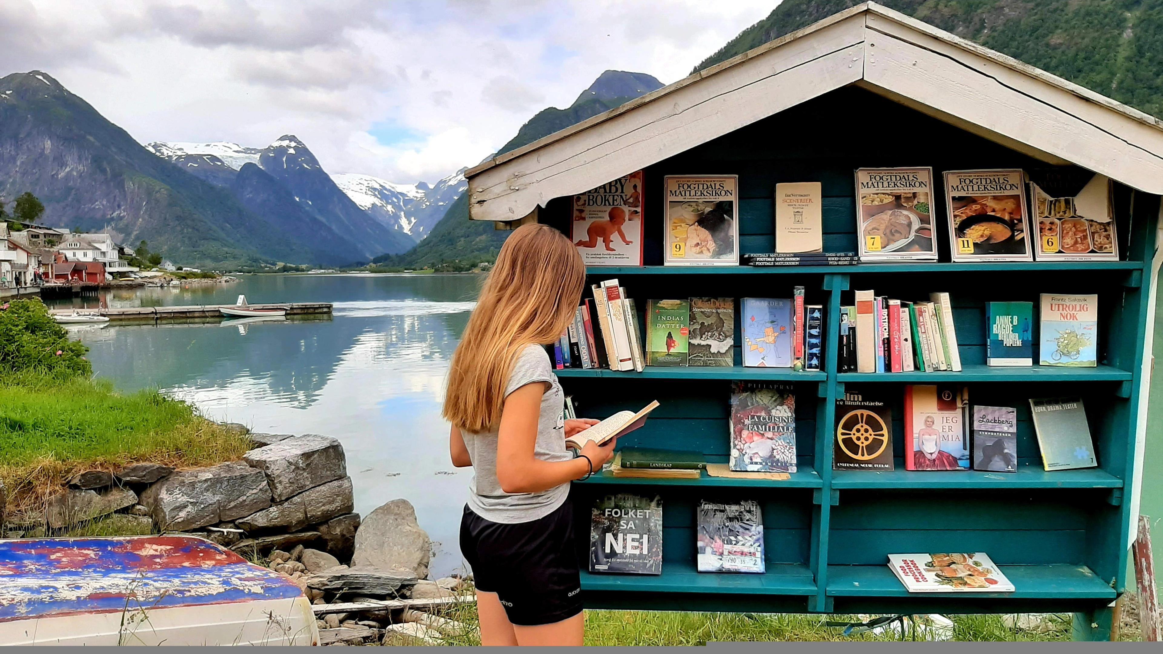 A girl looking at books by an outdoor bookshelf in Fjærland in Fjord Norway, one of Norway's book towns