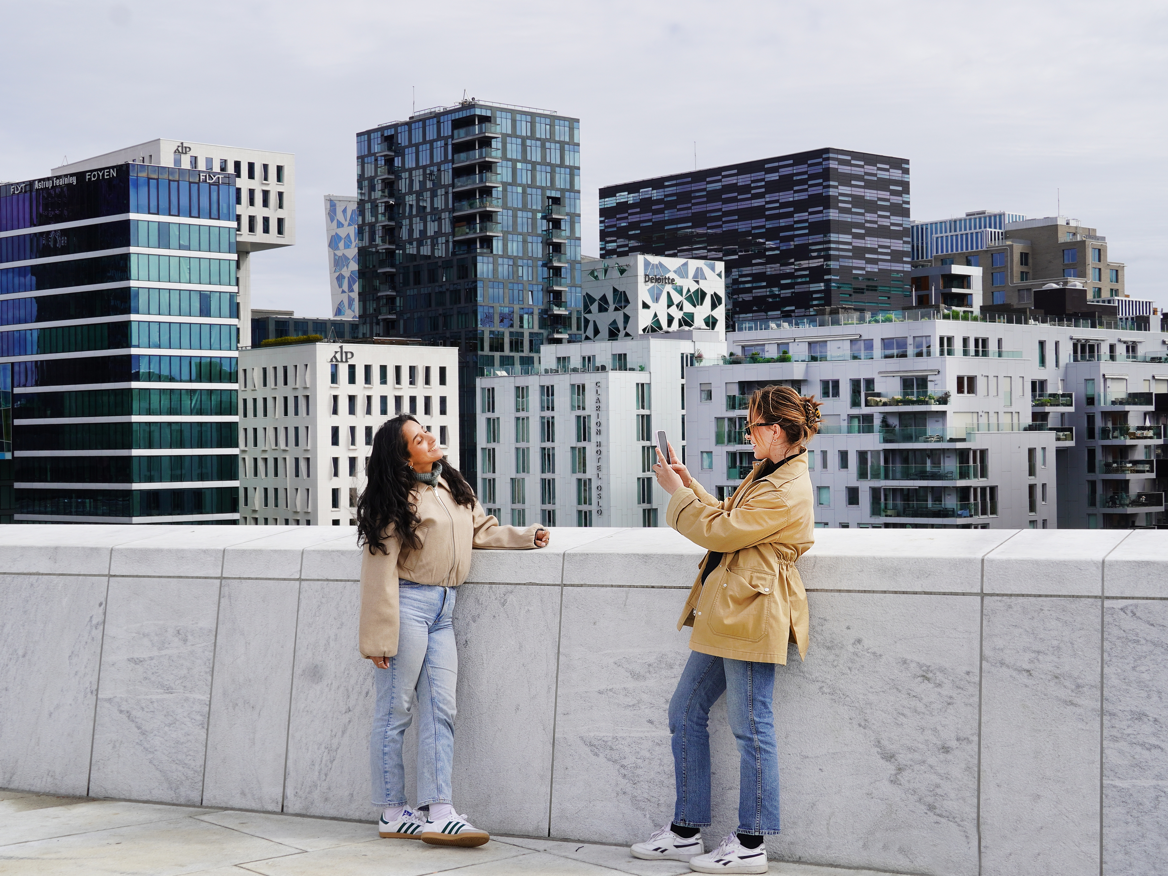 Two young women standing on the rooftop of the Oslo Opera House in Norway, capturing a photo with the city skyline in the background.
