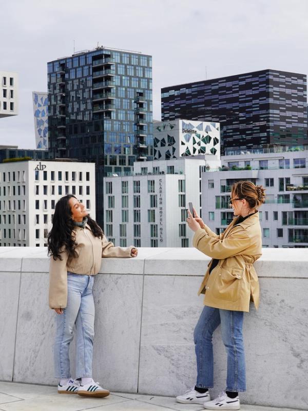 Two young women standing on the rooftop of the Oslo Opera House in Norway, capturing a photo with the city skyline in the background.