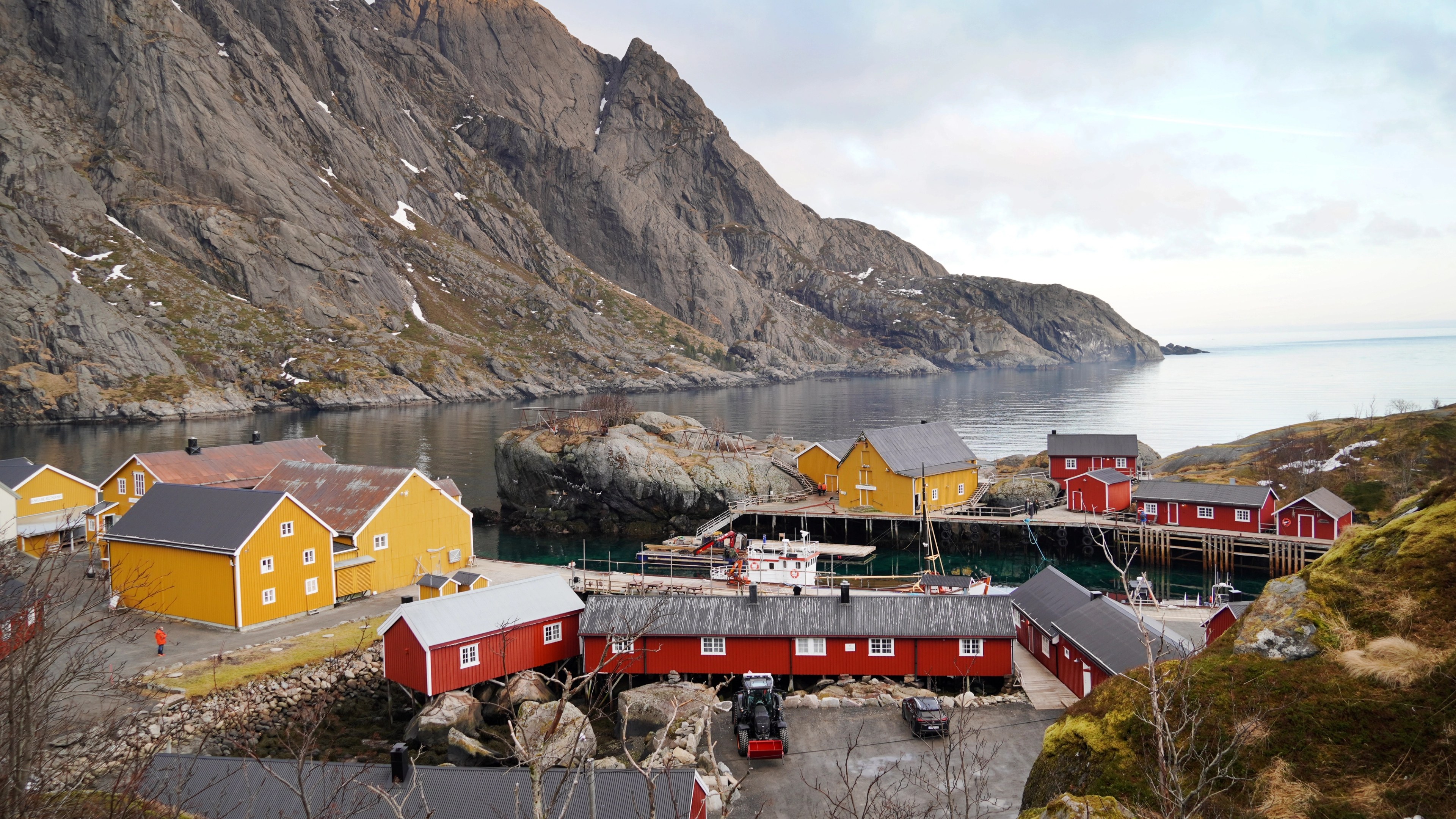 Red and yellow fisherman cabins below a mountain, by the sea.