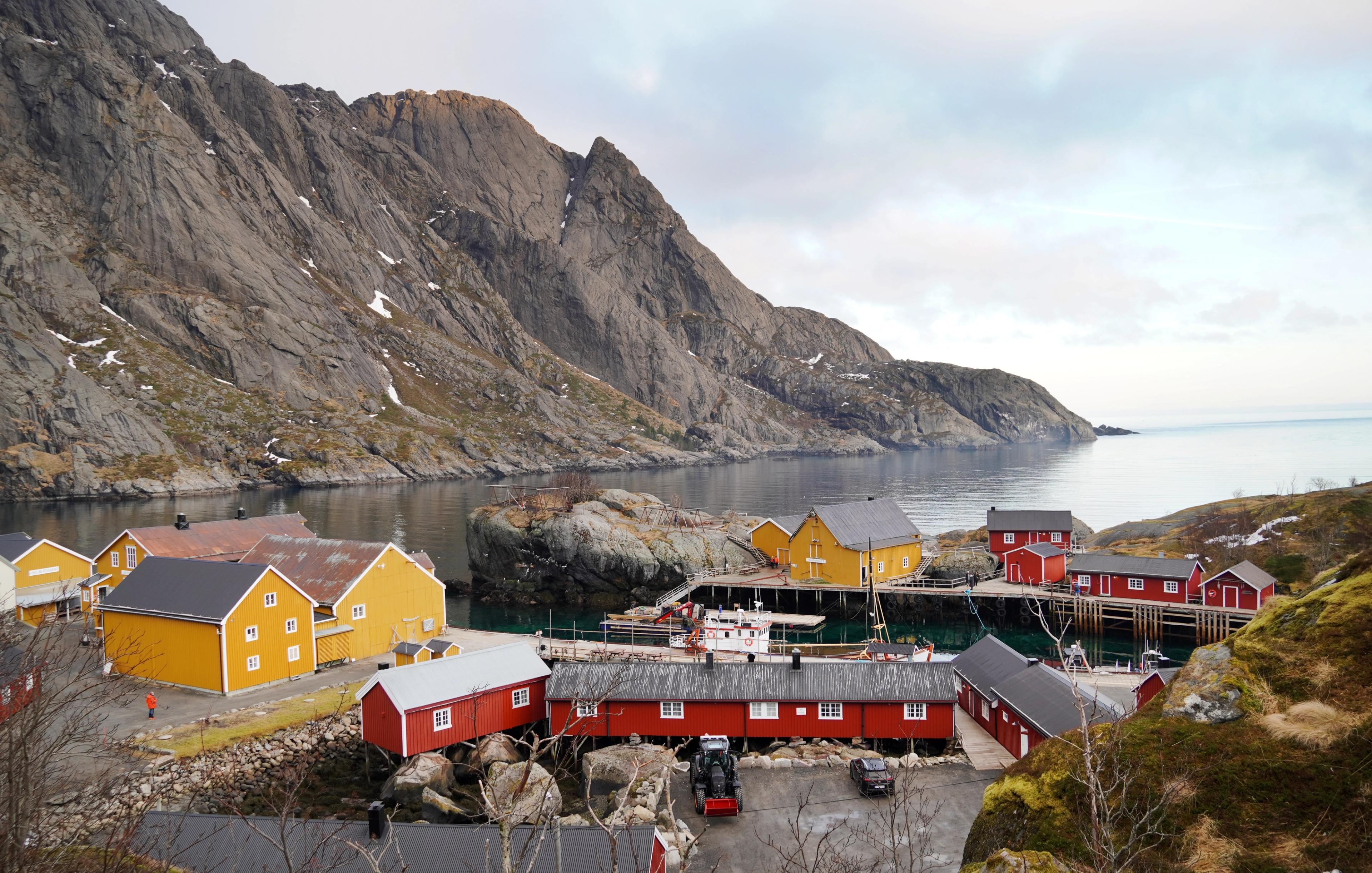 Red and yellow fisherman cabins below a mountain, by the sea.
