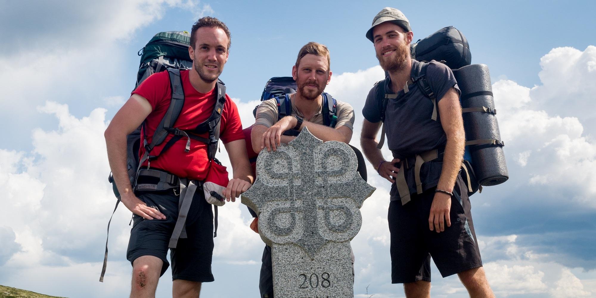 Three men standing around a milestone on the pilgrimage path to Trondheim, Norway