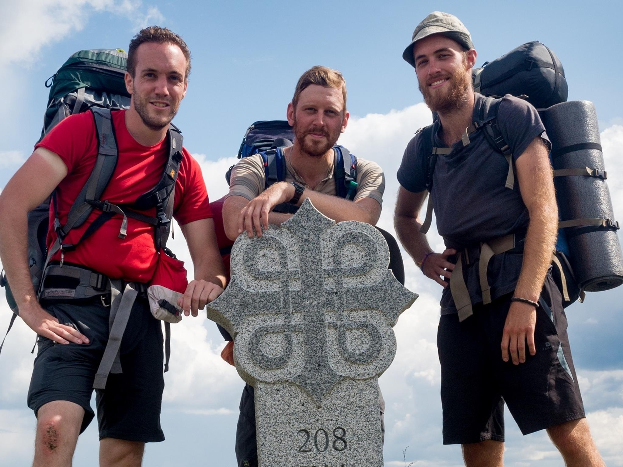Three men standing around a milestone on the pilgrimage path to Trondheim, Norway
