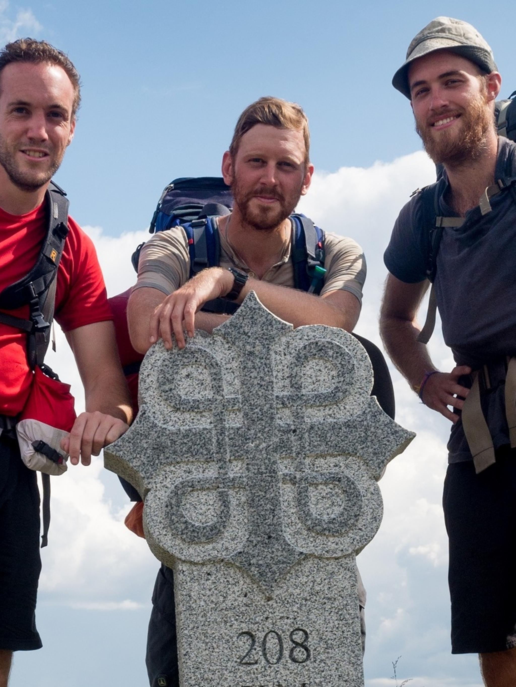 Three men standing around a milestone on the pilgrimage path to Trondheim, Norway