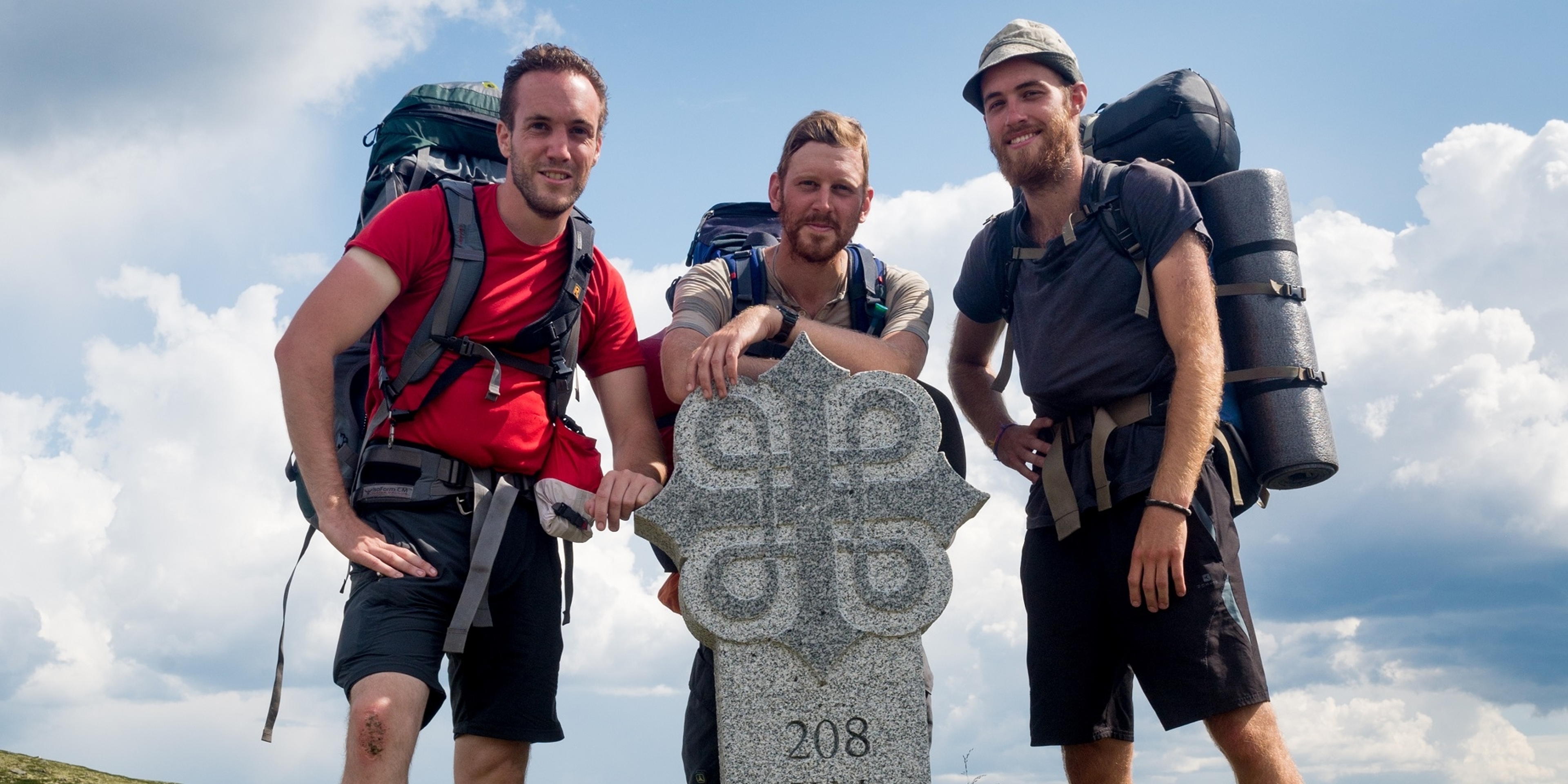 Three men standing around a milestone on the pilgrimage path to Trondheim, Norway