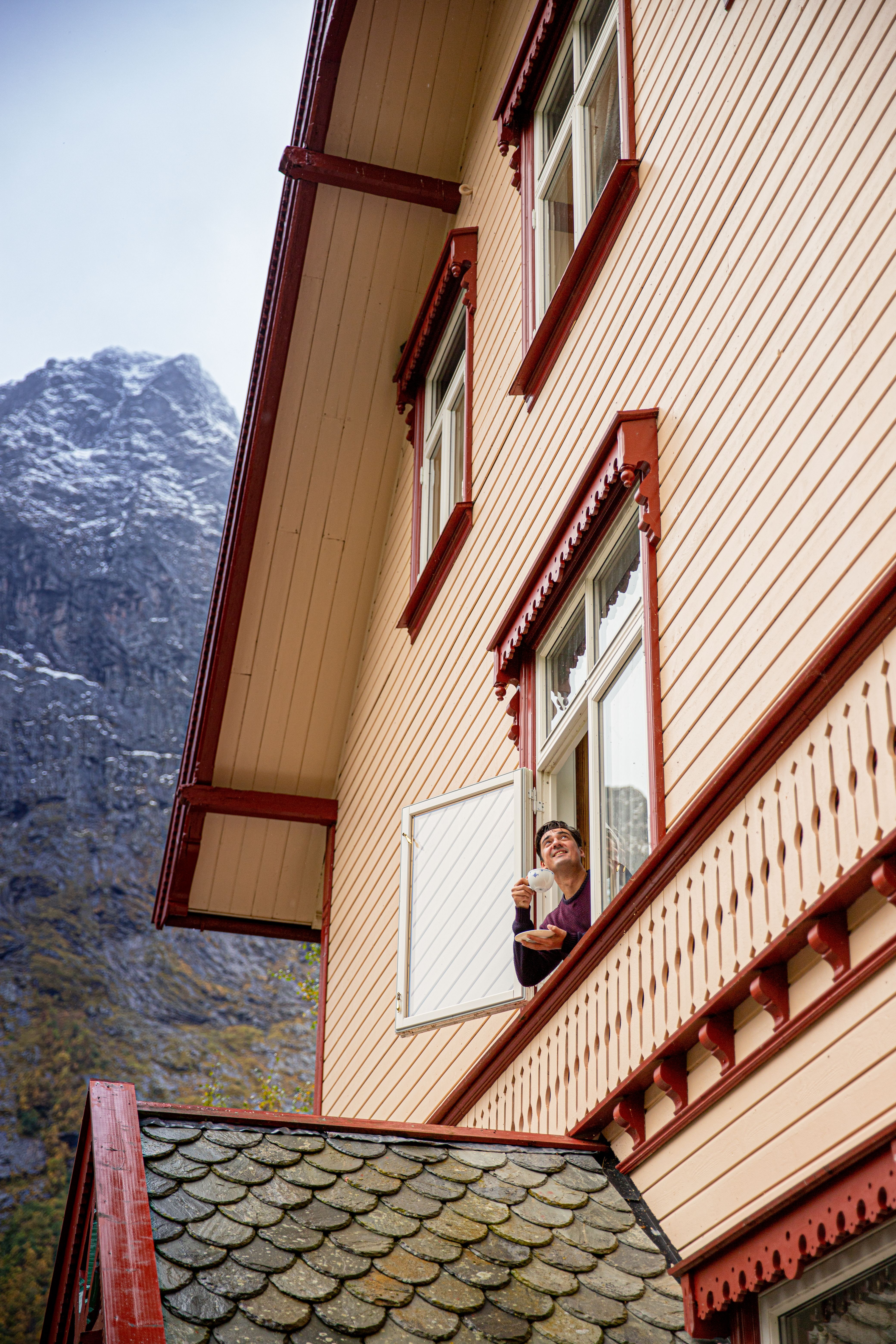 Een man kijkt uit een raam in het Hotel Union Øye aan het Hjørundfjord in Fjord-Noorwegen