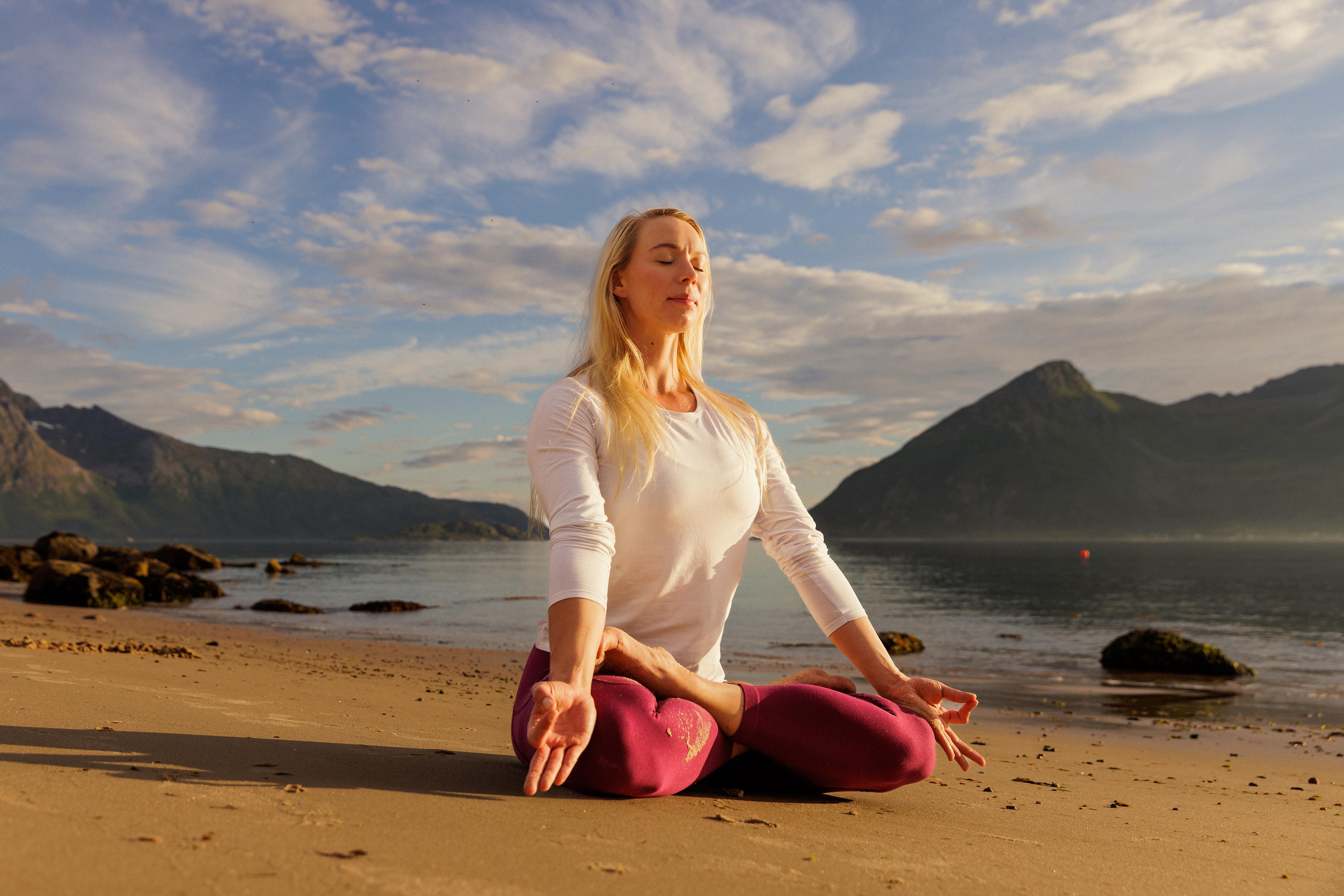 A woman sitting in lotus yoga position on the beach in the midnight sun, Northern Norway.