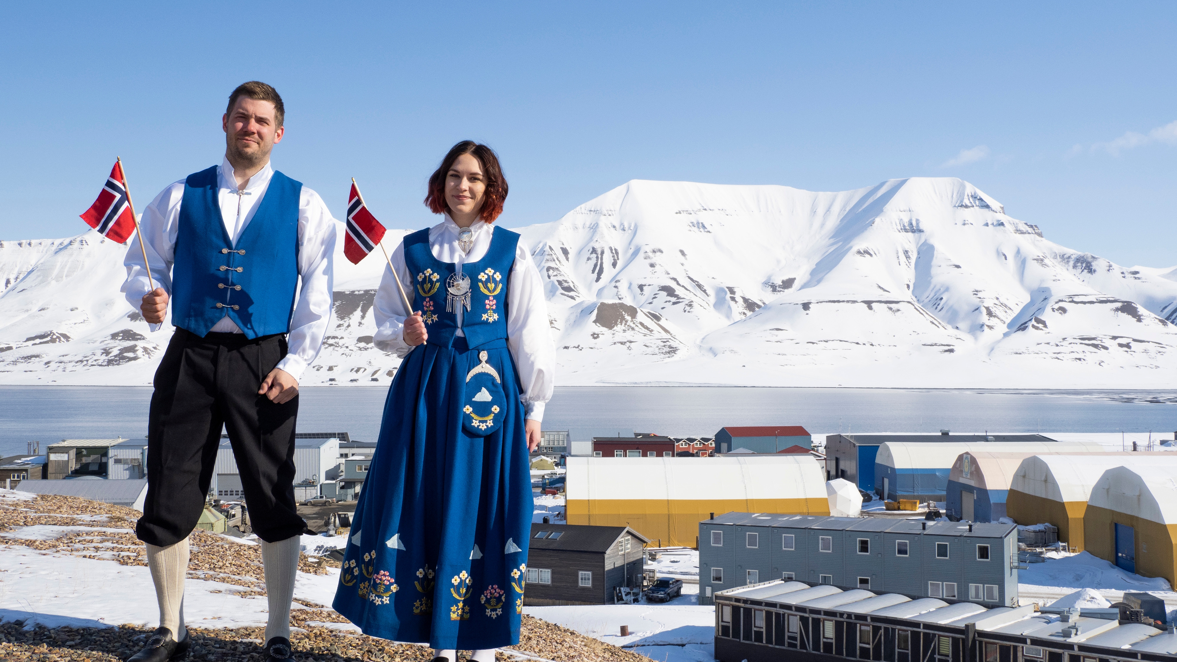 Ei dame og en mann iført Svalbardbunad med Longyearbyen i bakgrunnen på Svalbard