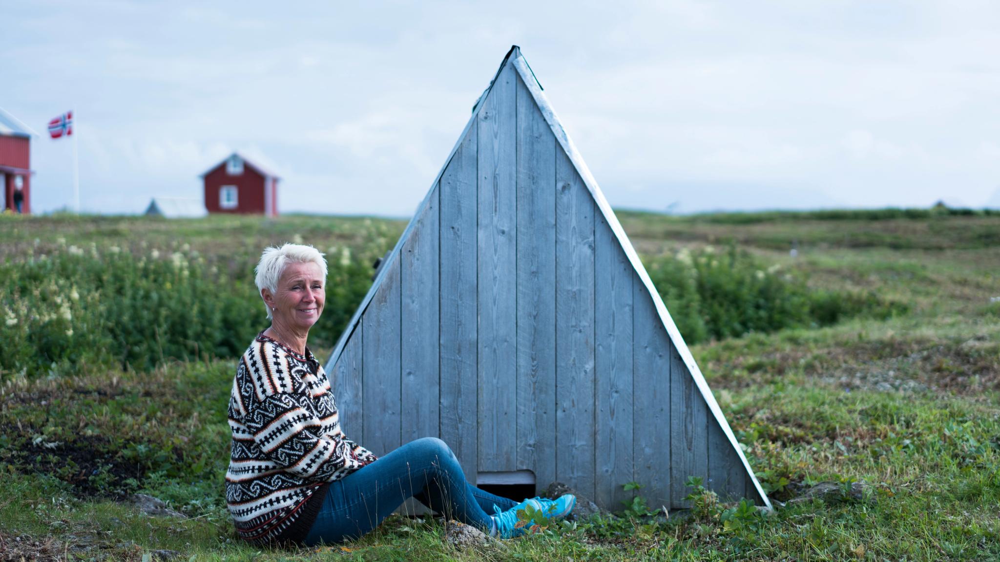 A woman sitting outside a 'house' for eider ducks, at Lånan in the Vega Islands, Nordland