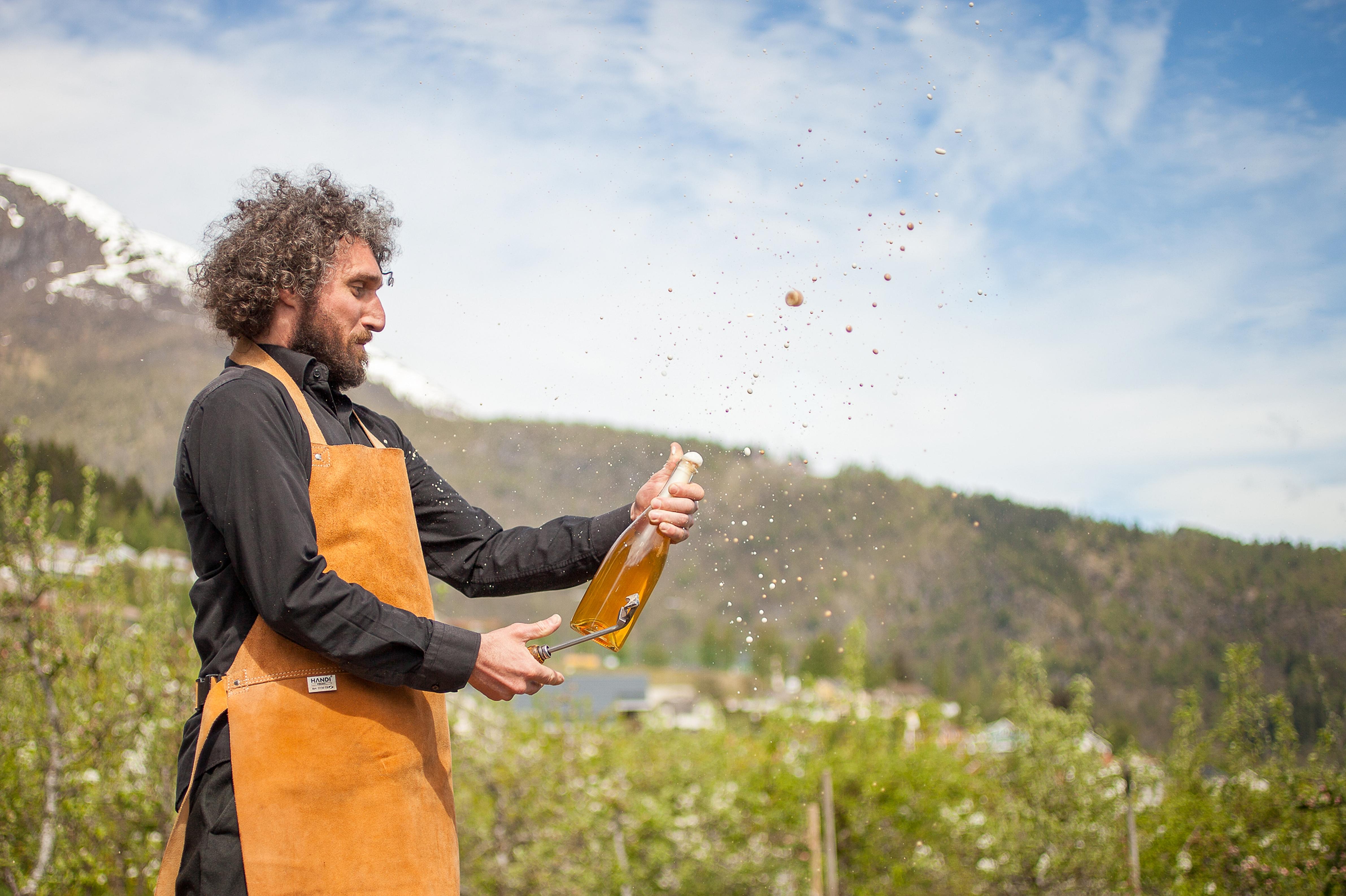 A man popping the cork of a bottle of cider in the beautiful nature around Ciderhuset, Fjord Norway