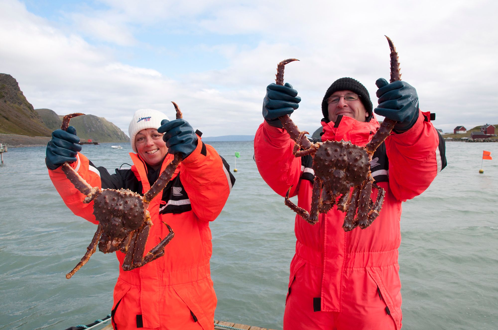 Two people holding up king crabs on a boat outside of Honningsvåg in Northern Norway