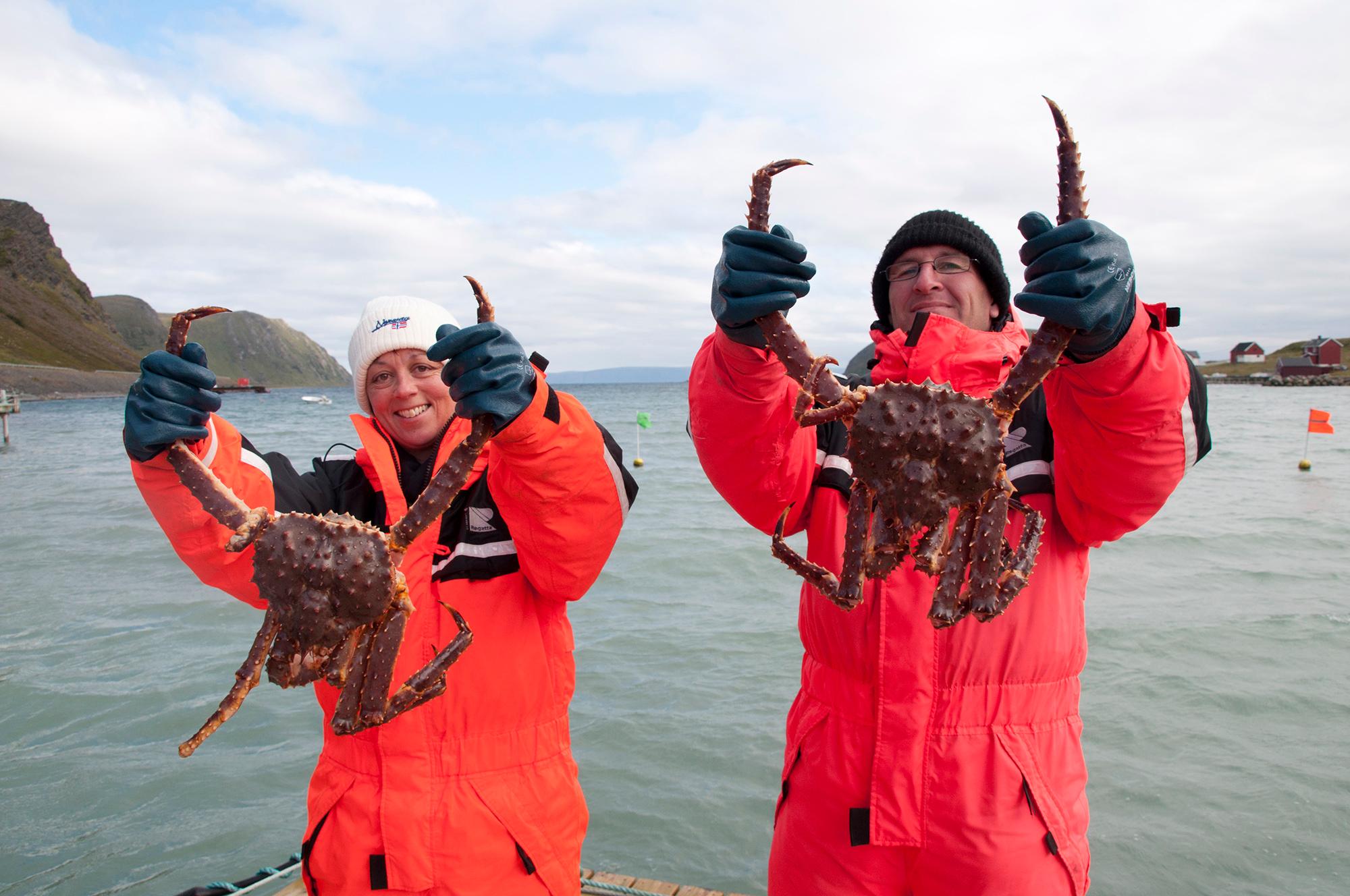 Two people holding up king crabs on a boat outside of Honningsvåg in Northern Norway