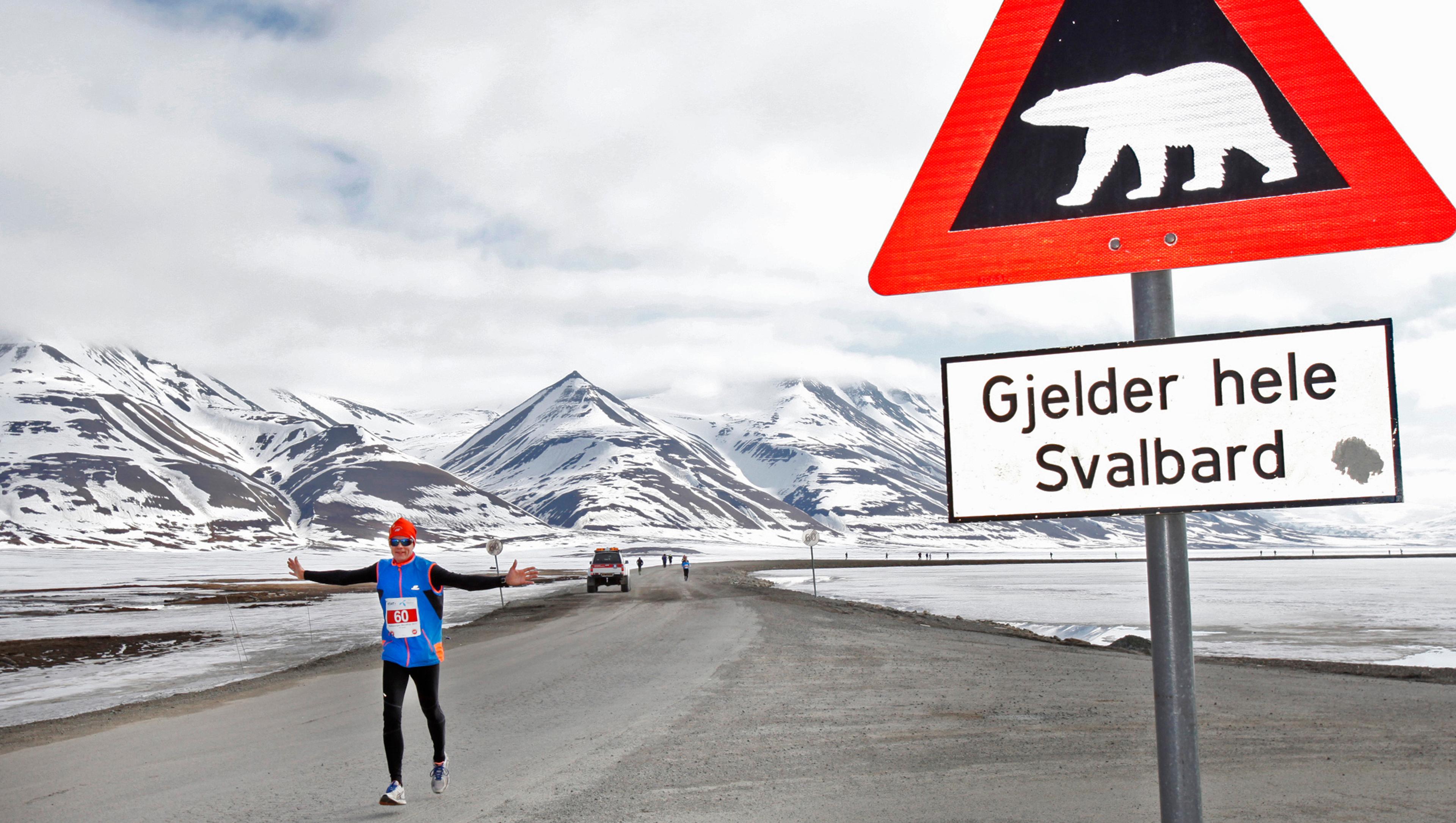 A marathon runner passing by a polar bear warning sign at Spitsbergen in Svalbard