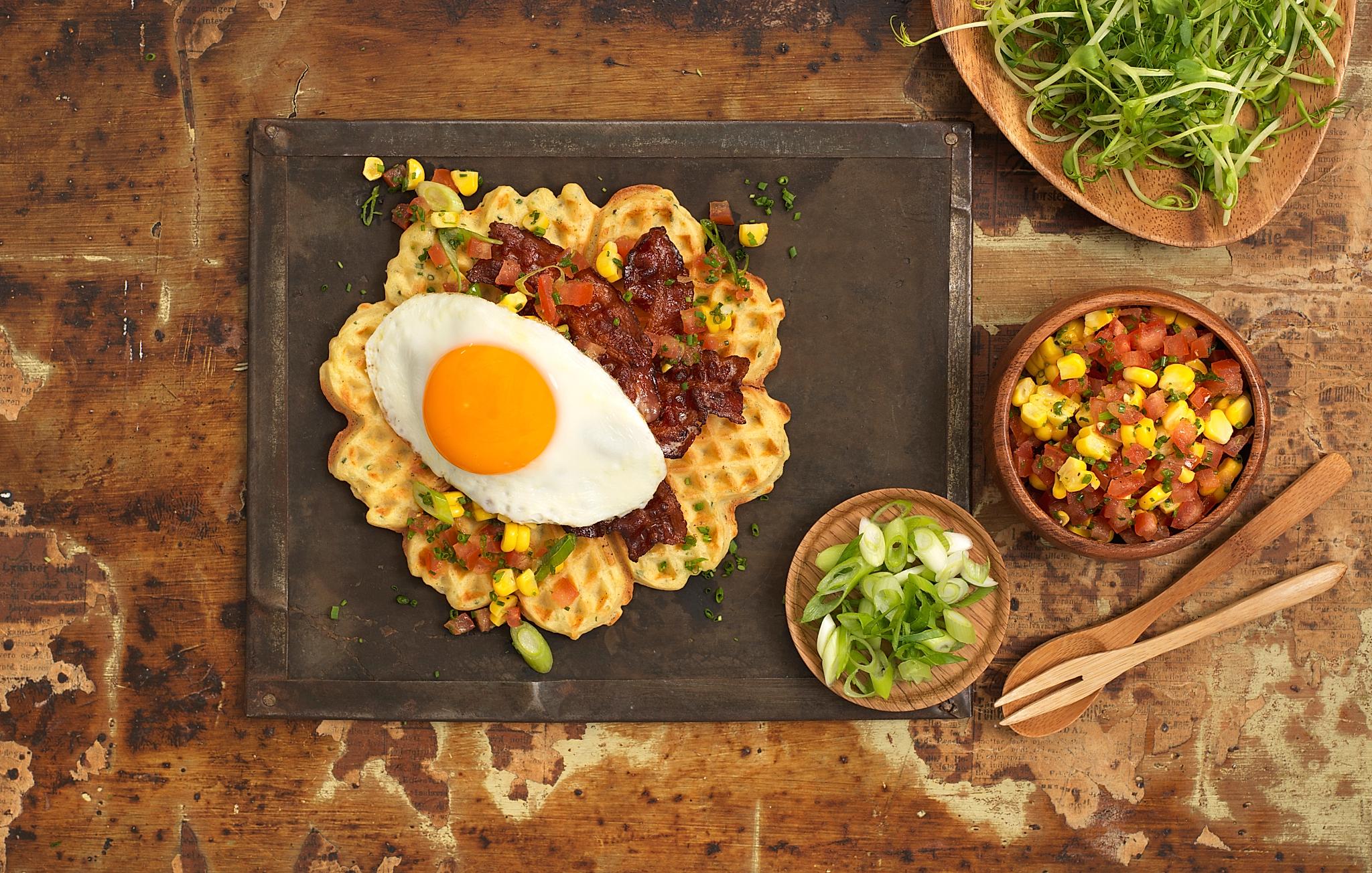 A plate with waffle with egg and bacon and some side dishes