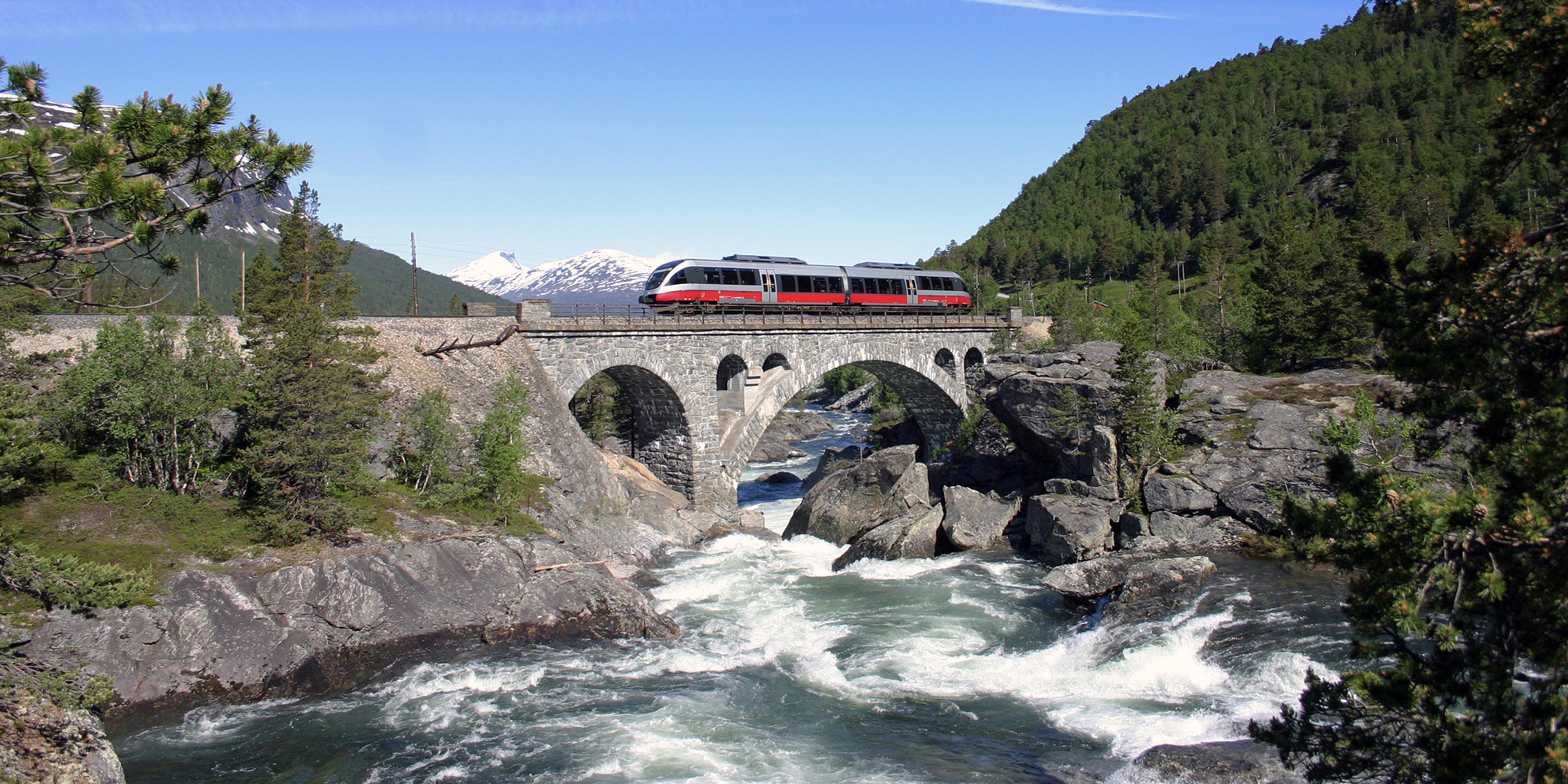 A train passes a river along the Rauma Railway, Norway