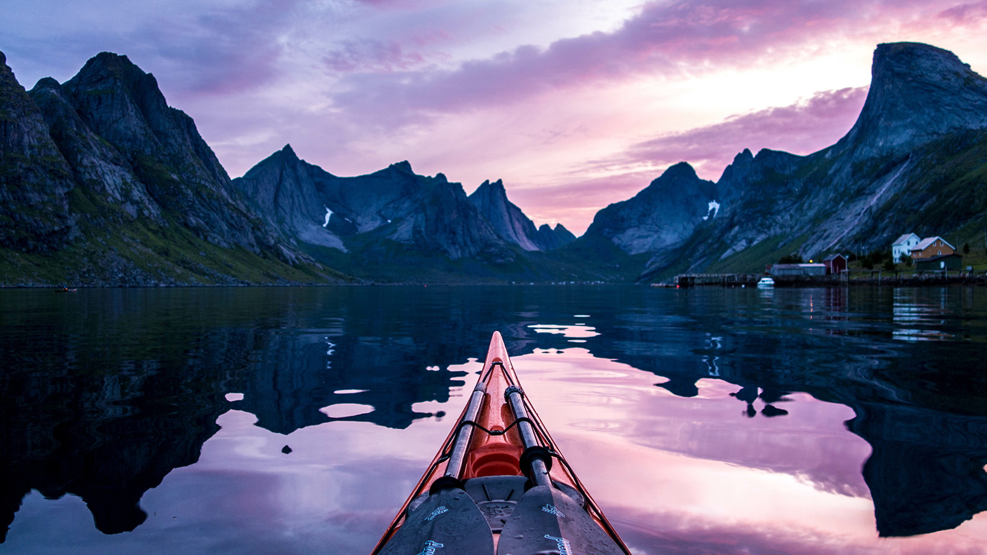Spidsen af en kajak og de stejle fjelde under midnatssolen i Moskenes på Lofoten, Nord-Norge
