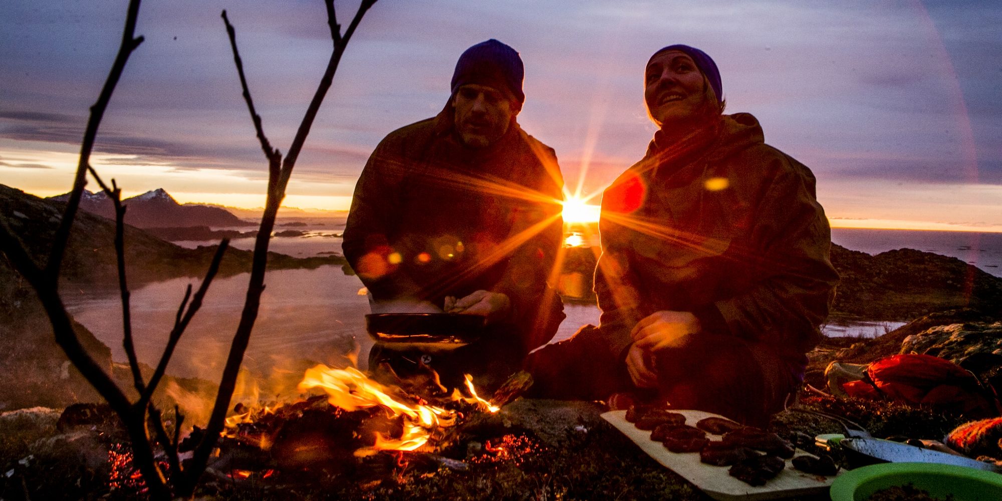 People cooking a meal outdoors over open fire during sunset