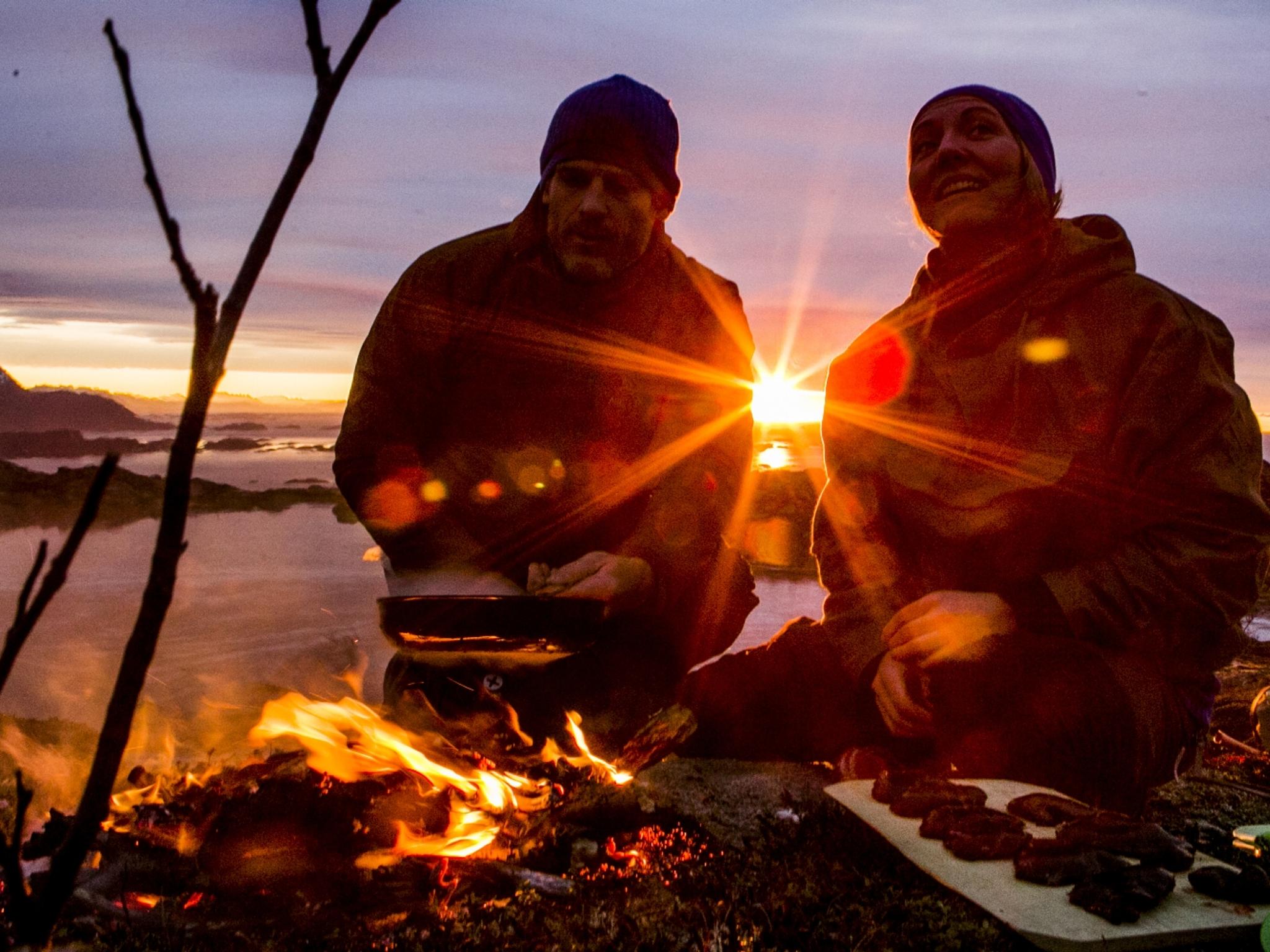 People cooking a meal outdoors over open fire during sunset