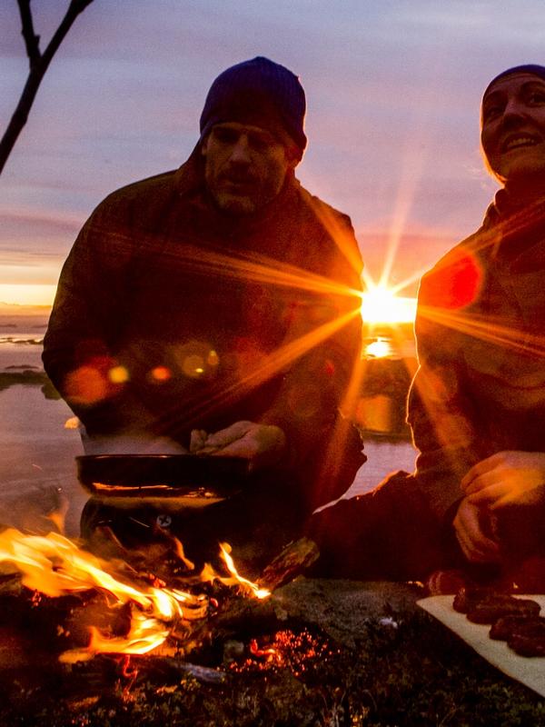 People cooking a meal outdoors over open fire during sunset