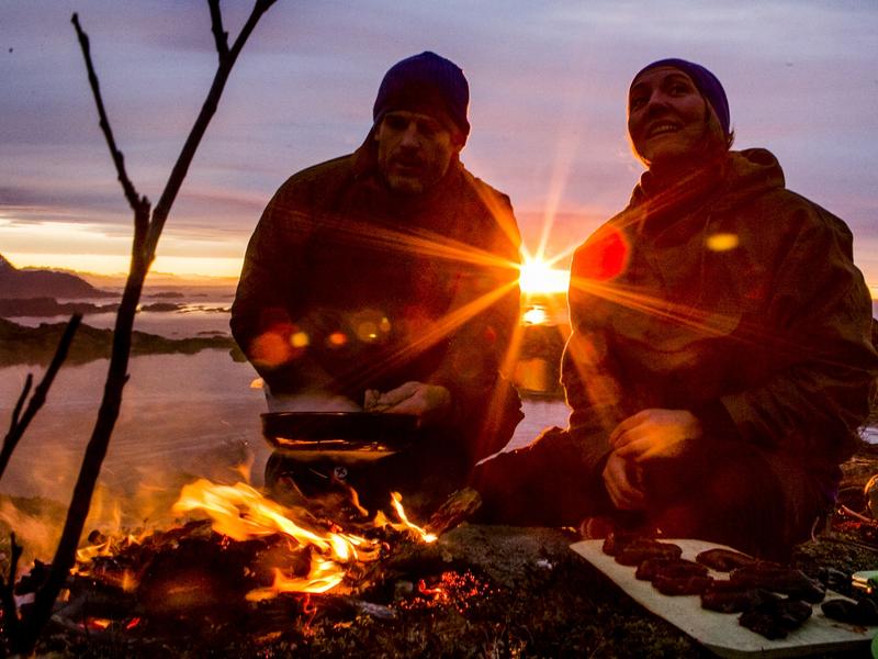 People cooking a meal outdoors over open fire during sunset