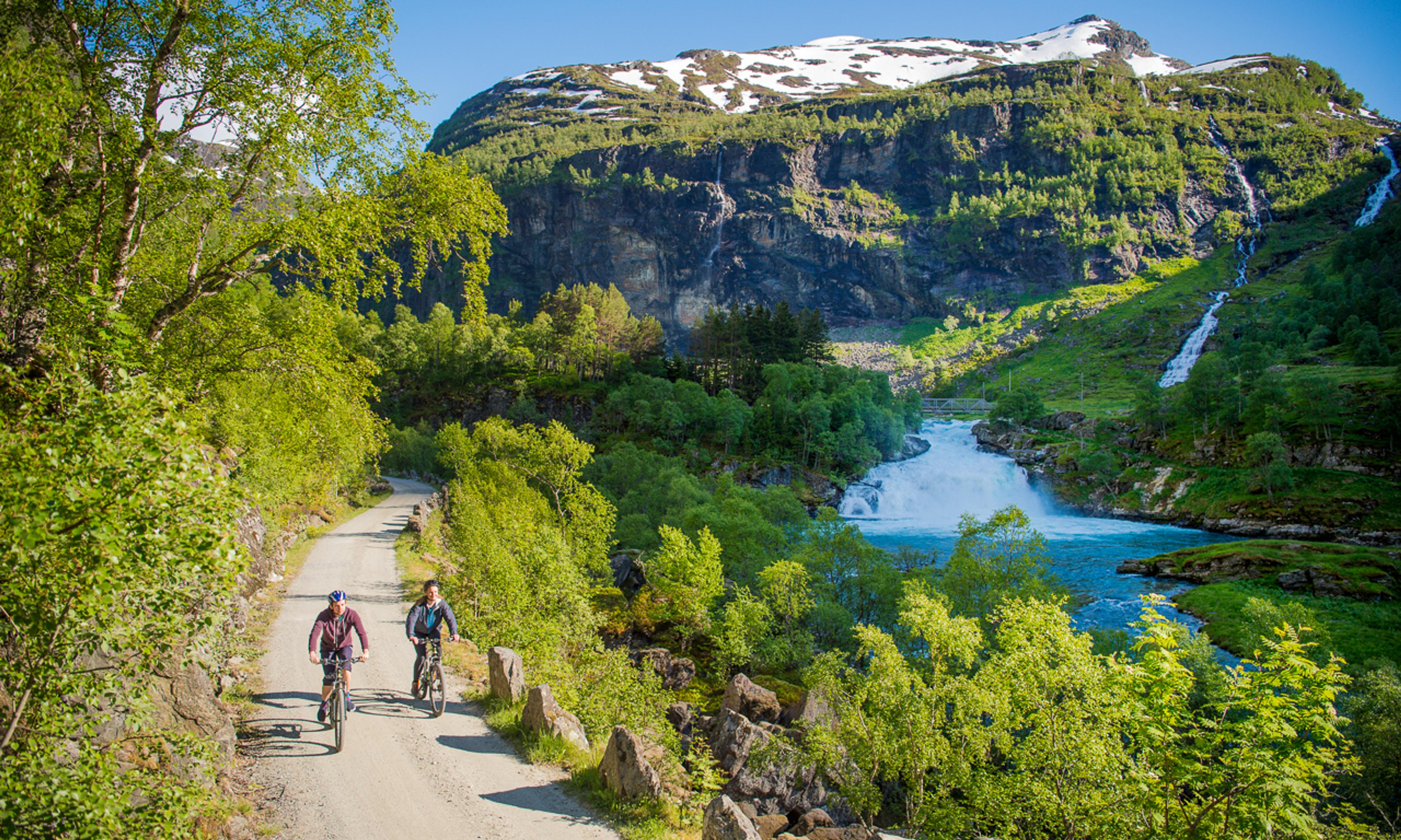 Two people biking down a trail next to a waterfall