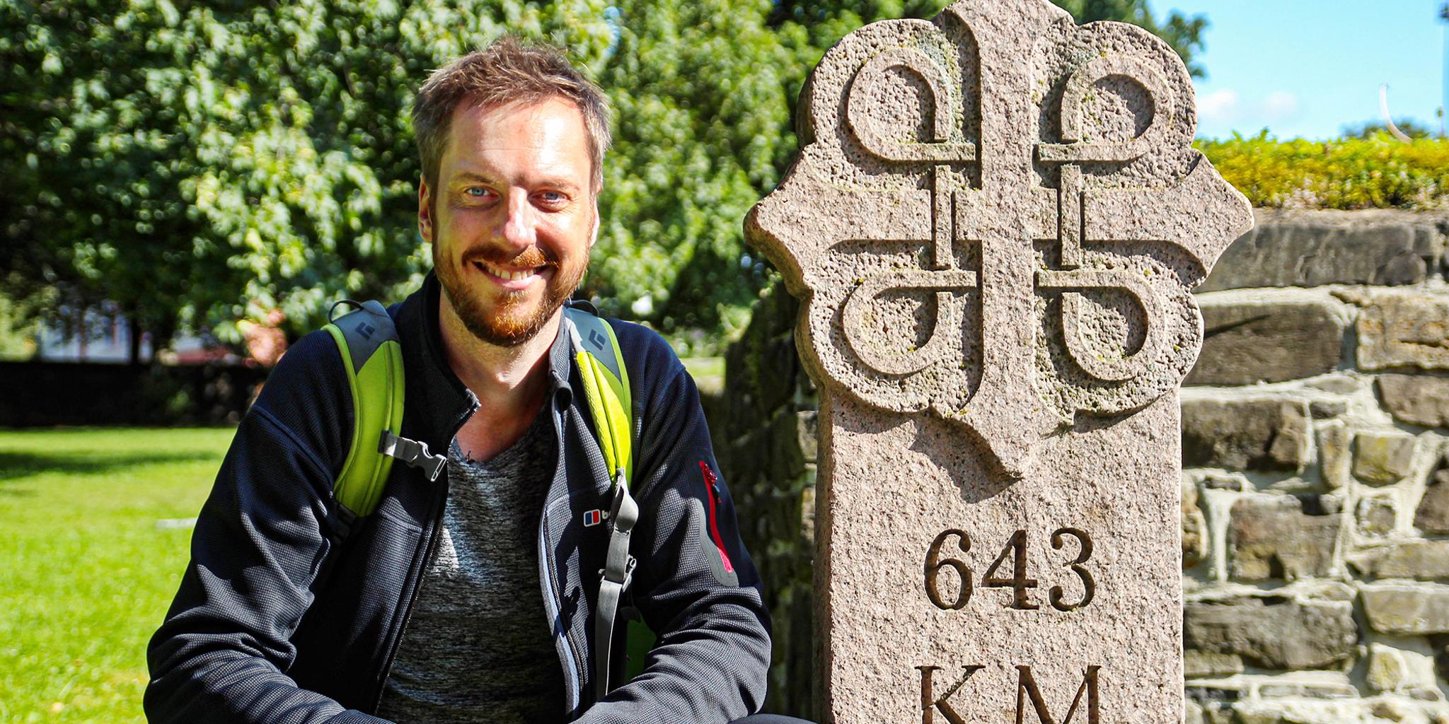 Pilgrimmen Kes Blans ved siden af et skilt, der markerer begyndelsen af Skt. Olavs-vejene fra Oslo til Trondheim, Norge