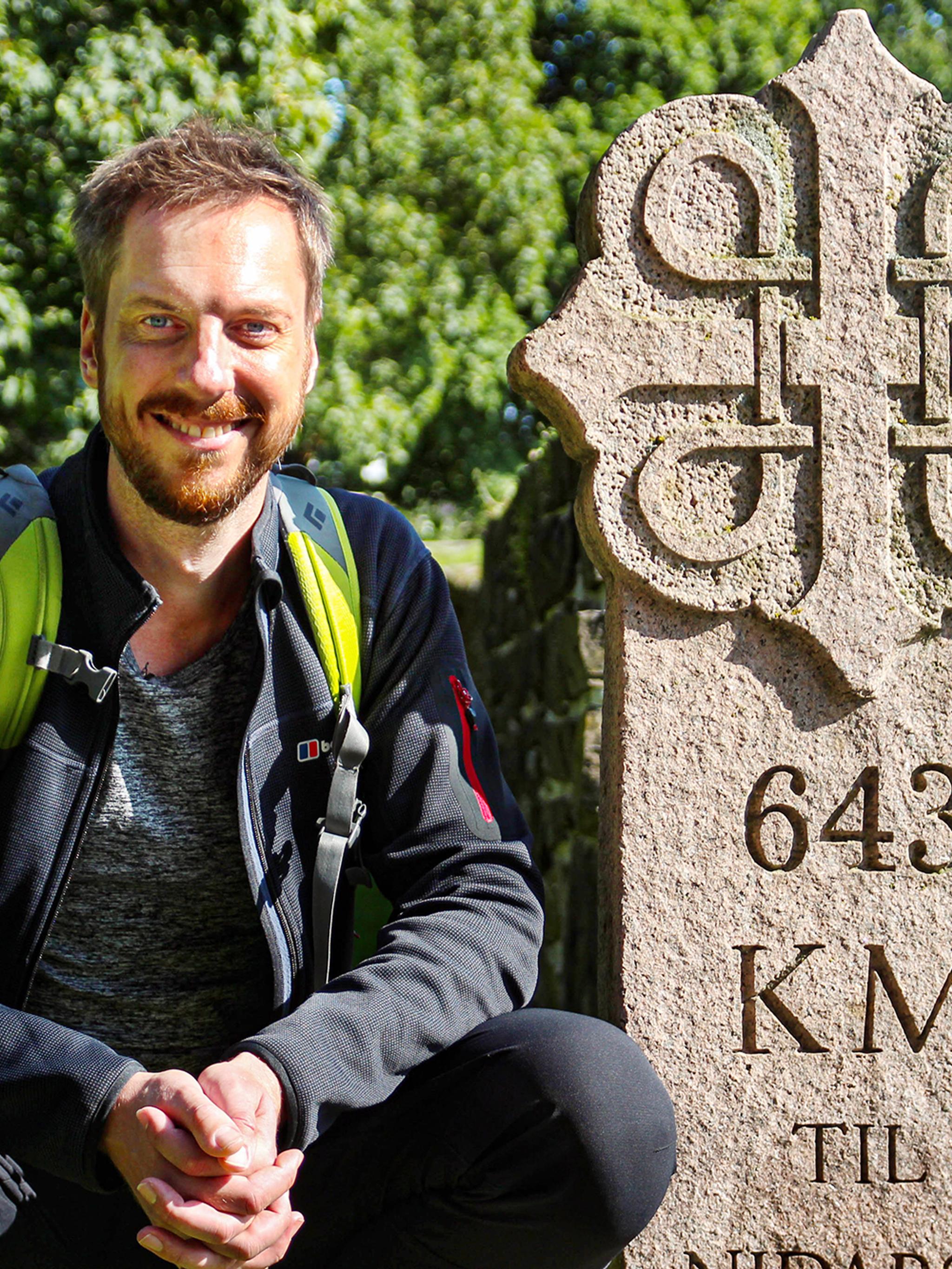 Pilgrimen Kes Blans bredvid en skylt som markerar början på pilgrimsvägen S:t Olavsleden från Oslo till Trondheim, Norge