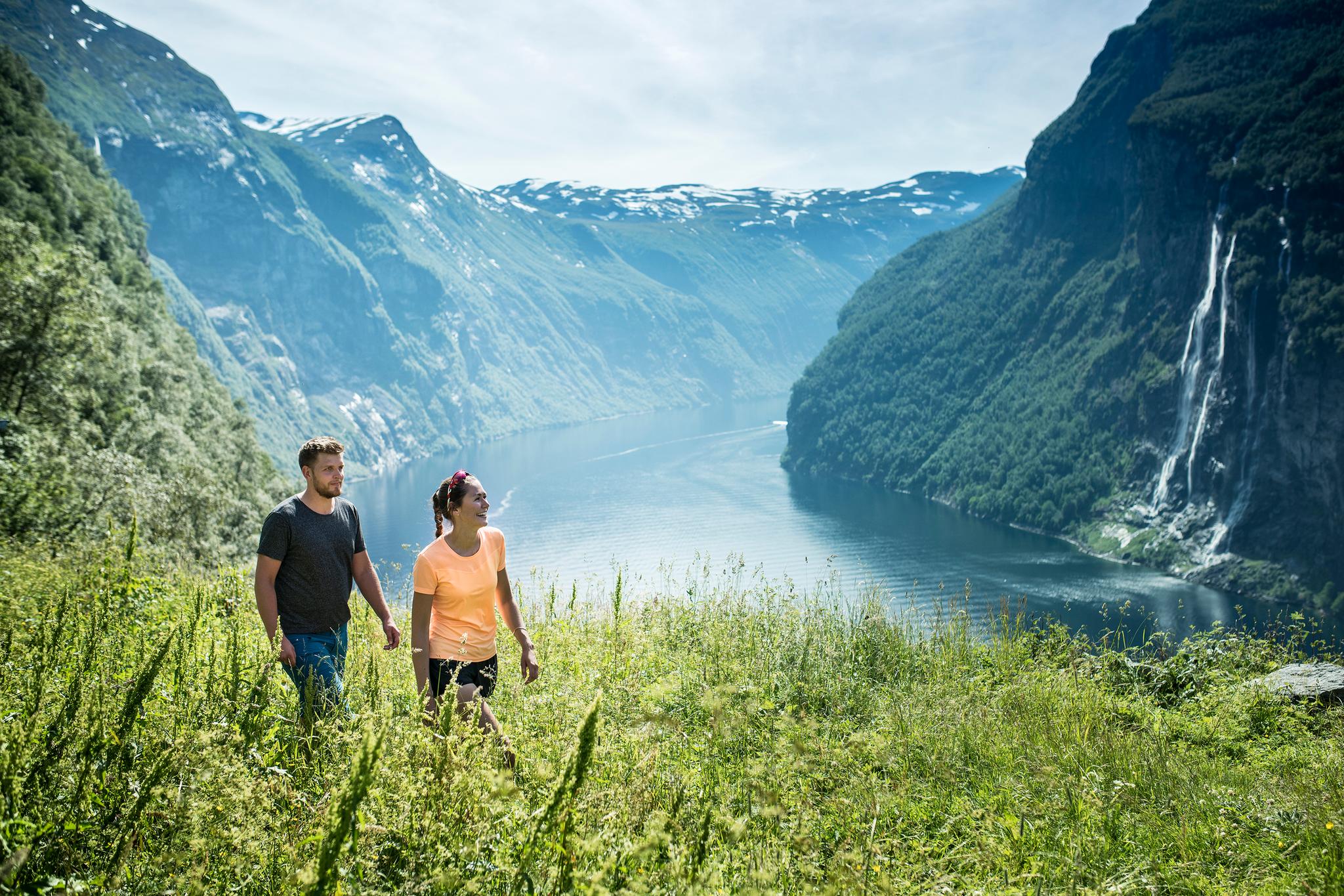 Couple hiking along fjord trail with view of majestic Norwegian landscape.