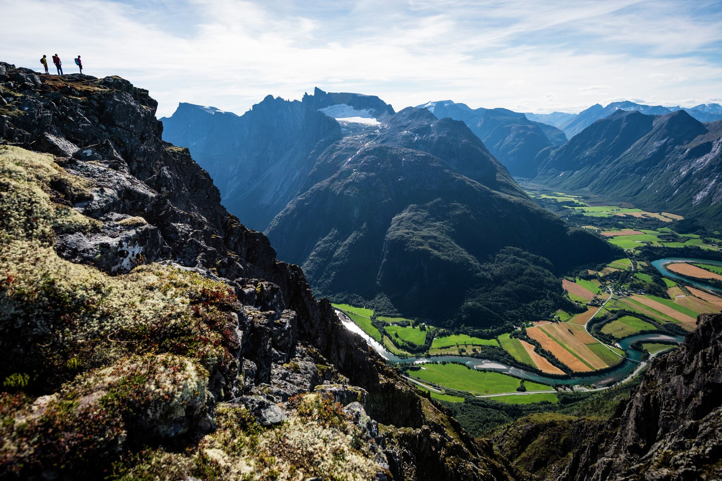 Three hikers seen looking out at the view from the Romsdalseggen ridge in Åndalsnes in Northwest, Fjord Norway