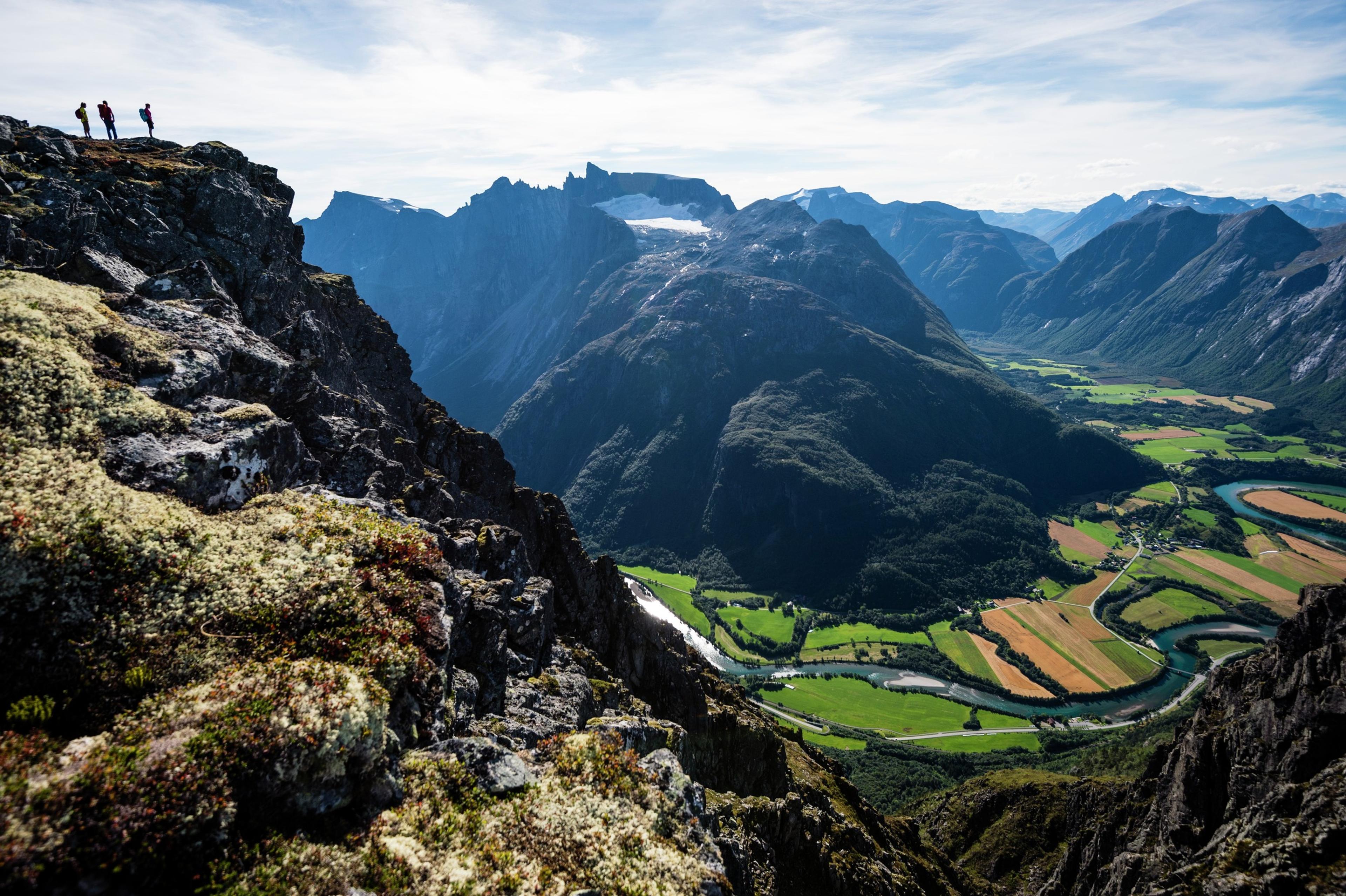 Three hikers seen looking out at the view from the Romsdalseggen ridge in Åndalsnes in Northwest, Fjord Norway